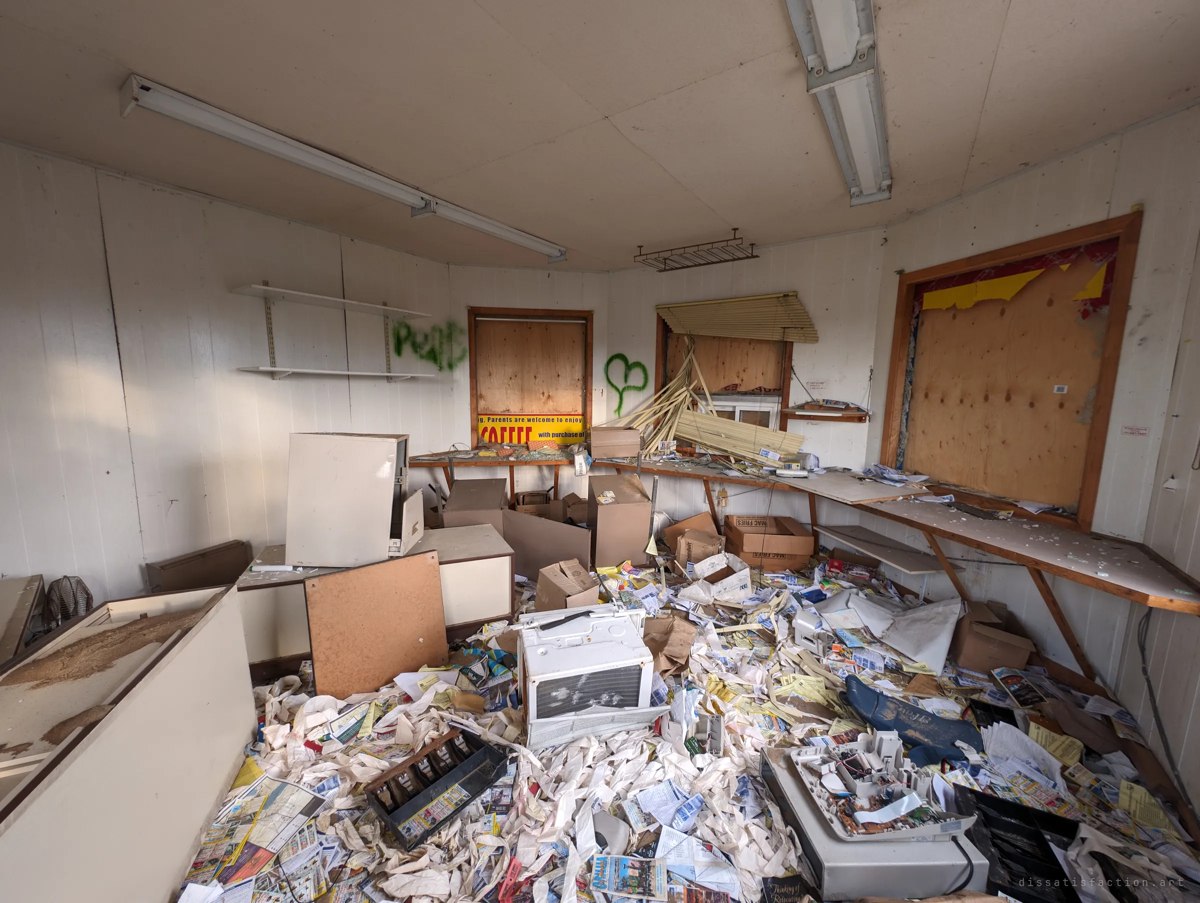 The inside of the booth buried in receipt paper, flyers, cash drawers and a toppled window air conditioner. Every window is boarded over and the counter is covered in glass.