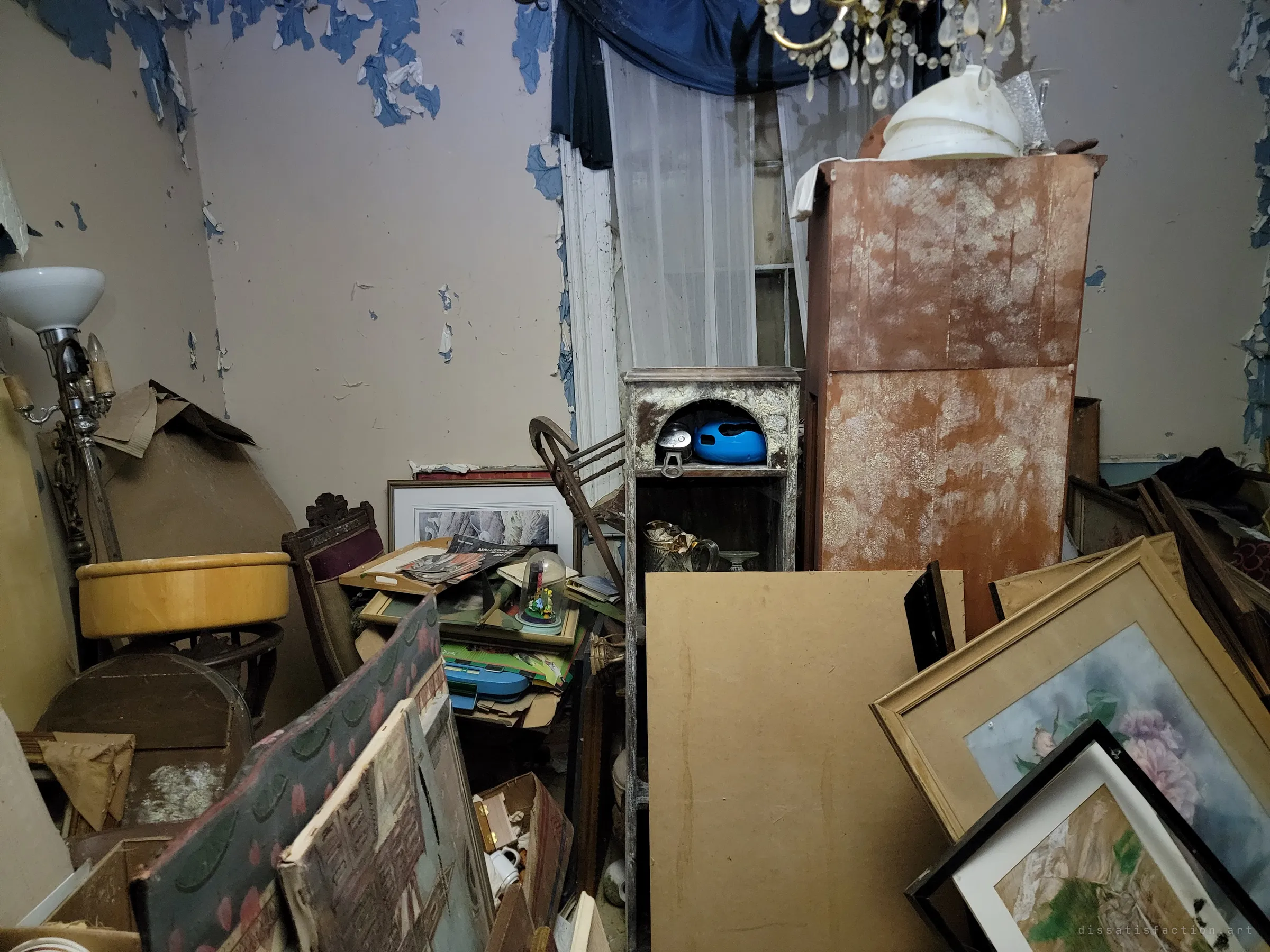 Peeling blue paint over a mauve wall frames a crystal chandelier, a mould-spotted wardrobe and stacks of leaning framed paintings. The fine furnishings slowly decaying in place give the house its faded grandeur.