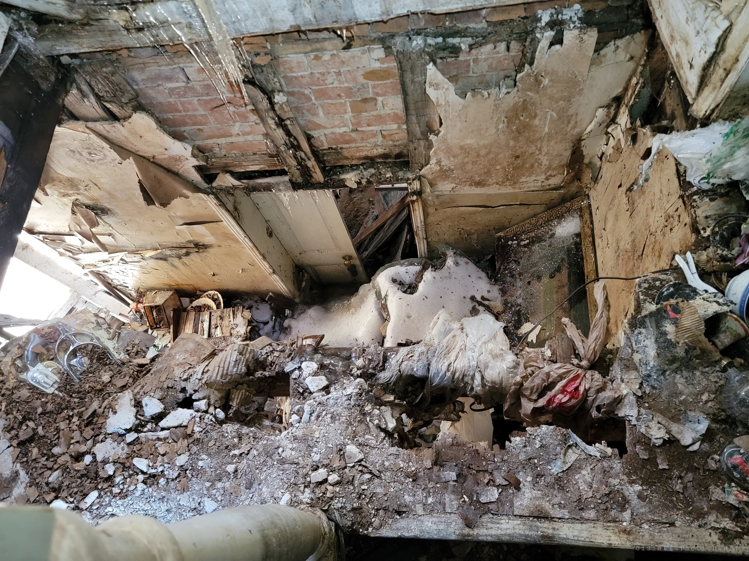Looking straight down through a collapsed floor into the room below, a drop of rubble, snow, torn plaster and exposed brick. It shows why the top of the stairs is effectively a dead end.