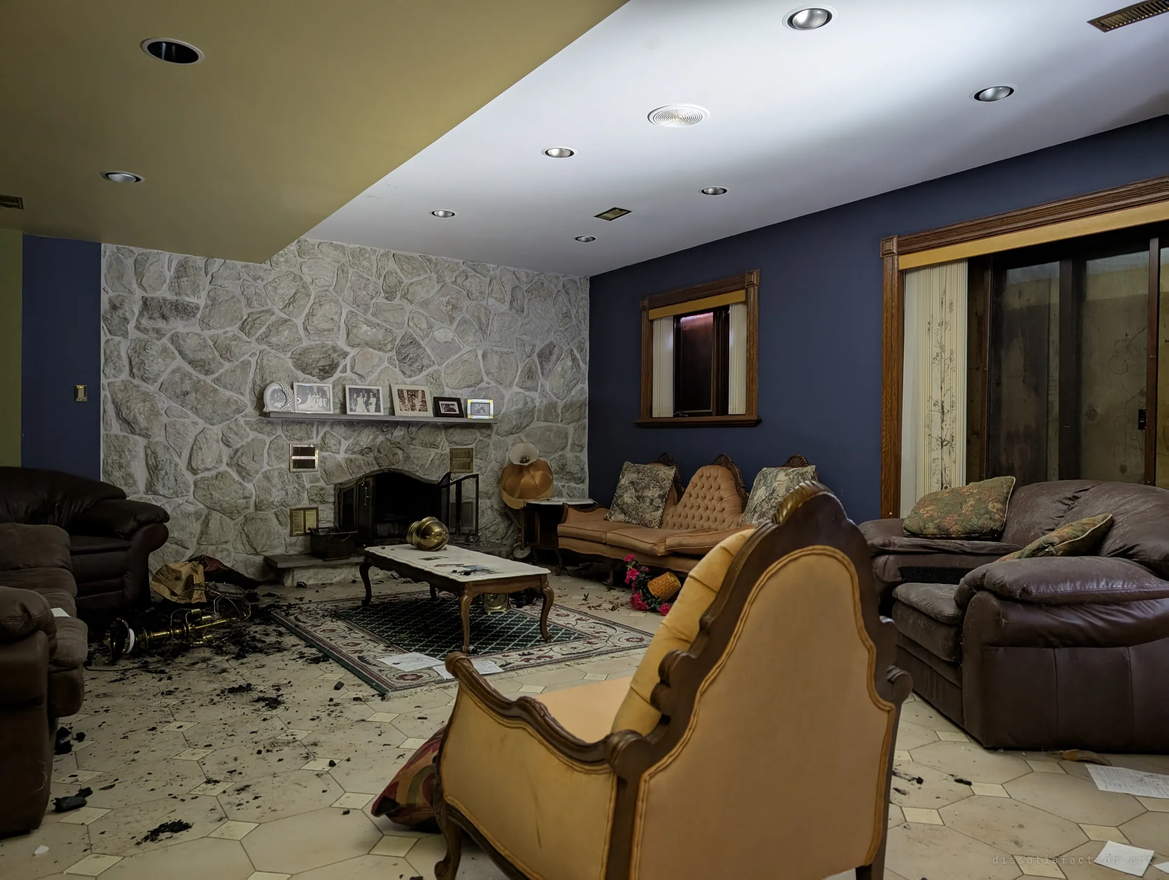 A wider view of the basement living room: leather sofas, a velvet armchair and the stone fireplace under recessed lights. Charcoal is trodden across the octagonal floor tiles.