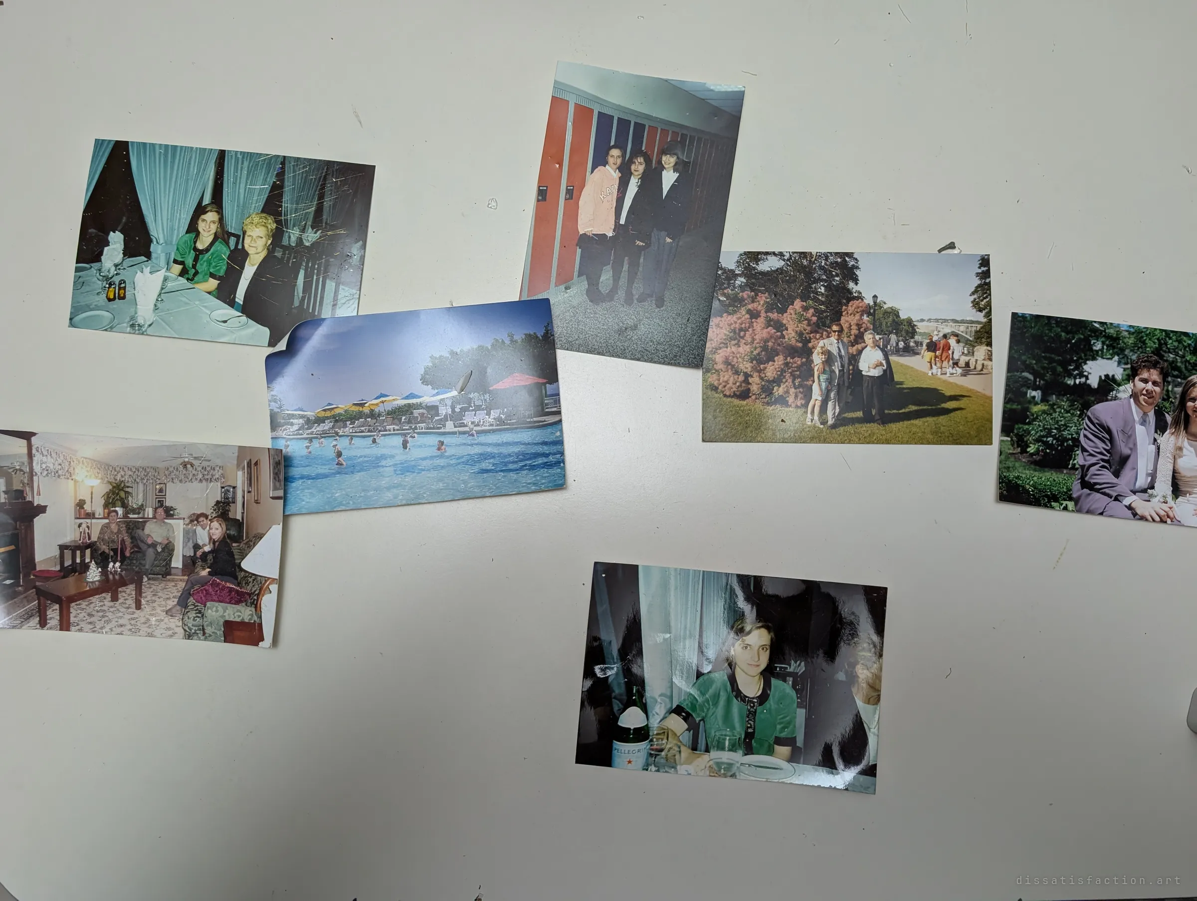 Old family prints of dinners, a pool holiday, a garden wedding and a living room are scattered across a white table, fragments of a family's history left behind.