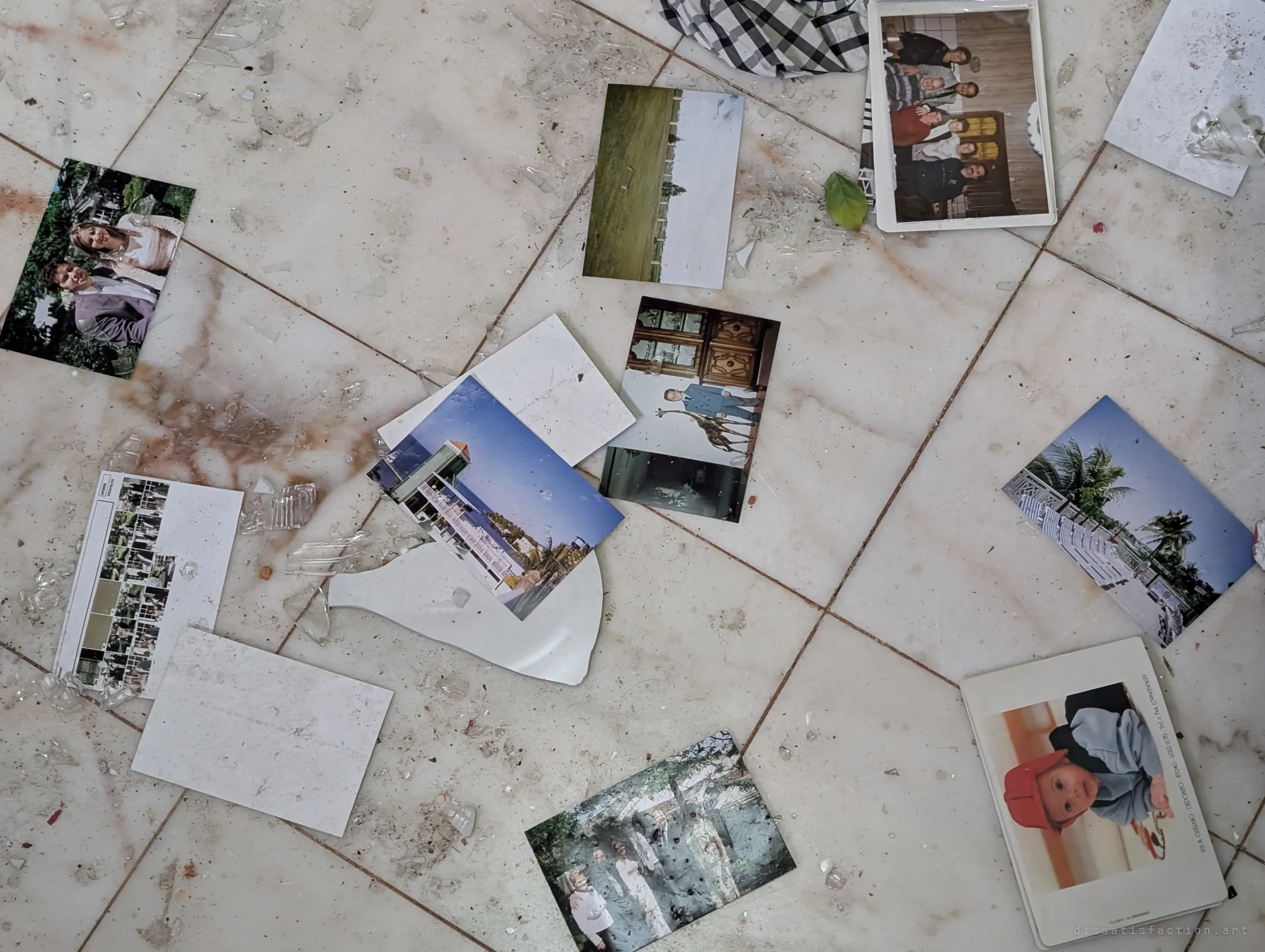 Family snapshots, a baby's studio portrait and blank photo backs lie among broken glass on a marble floor.