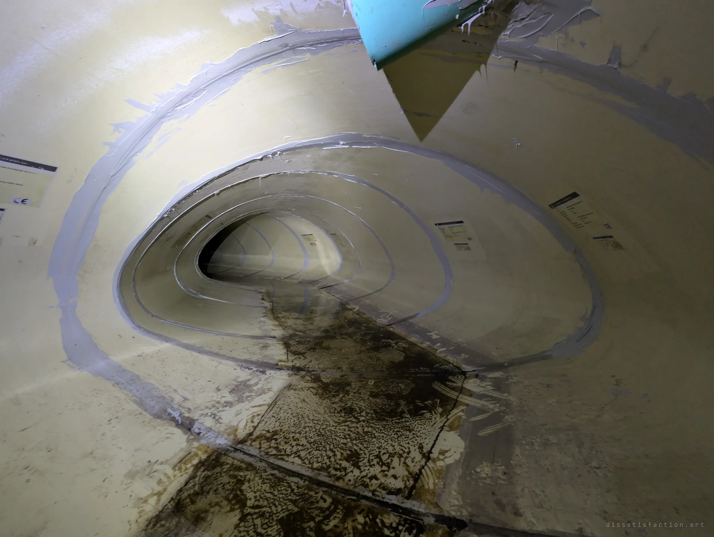 A torch-lit view down the liner pipe, its grey-sealed joints nesting like rings, with a torn piece of plastic hanging from the crown at the entrance.