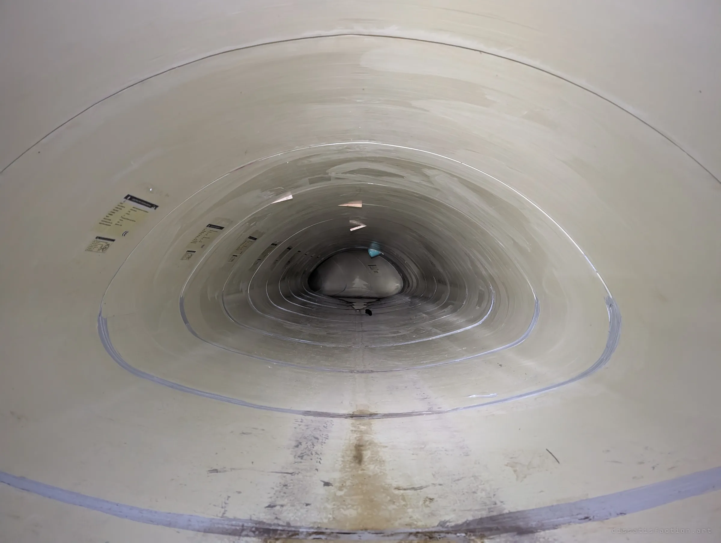 A clean, symmetrical view down the pale liner pipe, joint after joint shrinking toward a dark vanishing point, small manufacturer labels dotting the wall.