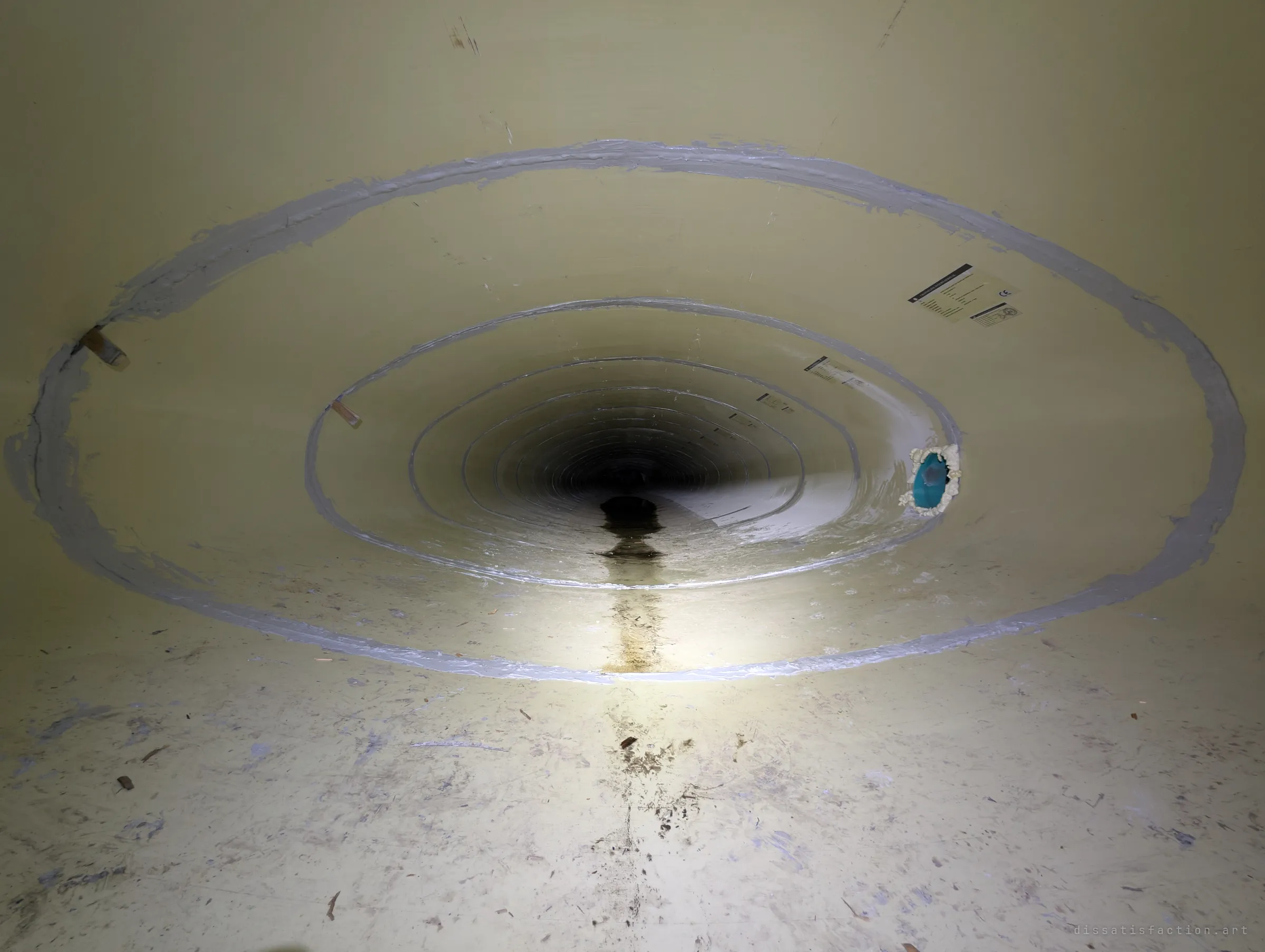 Looking down the inside of the cream fibreglass liner, grey sealant rings mark each joint as they shrink toward a dark vanishing point. A small blue-plugged opening breaks the smooth wall on the right.