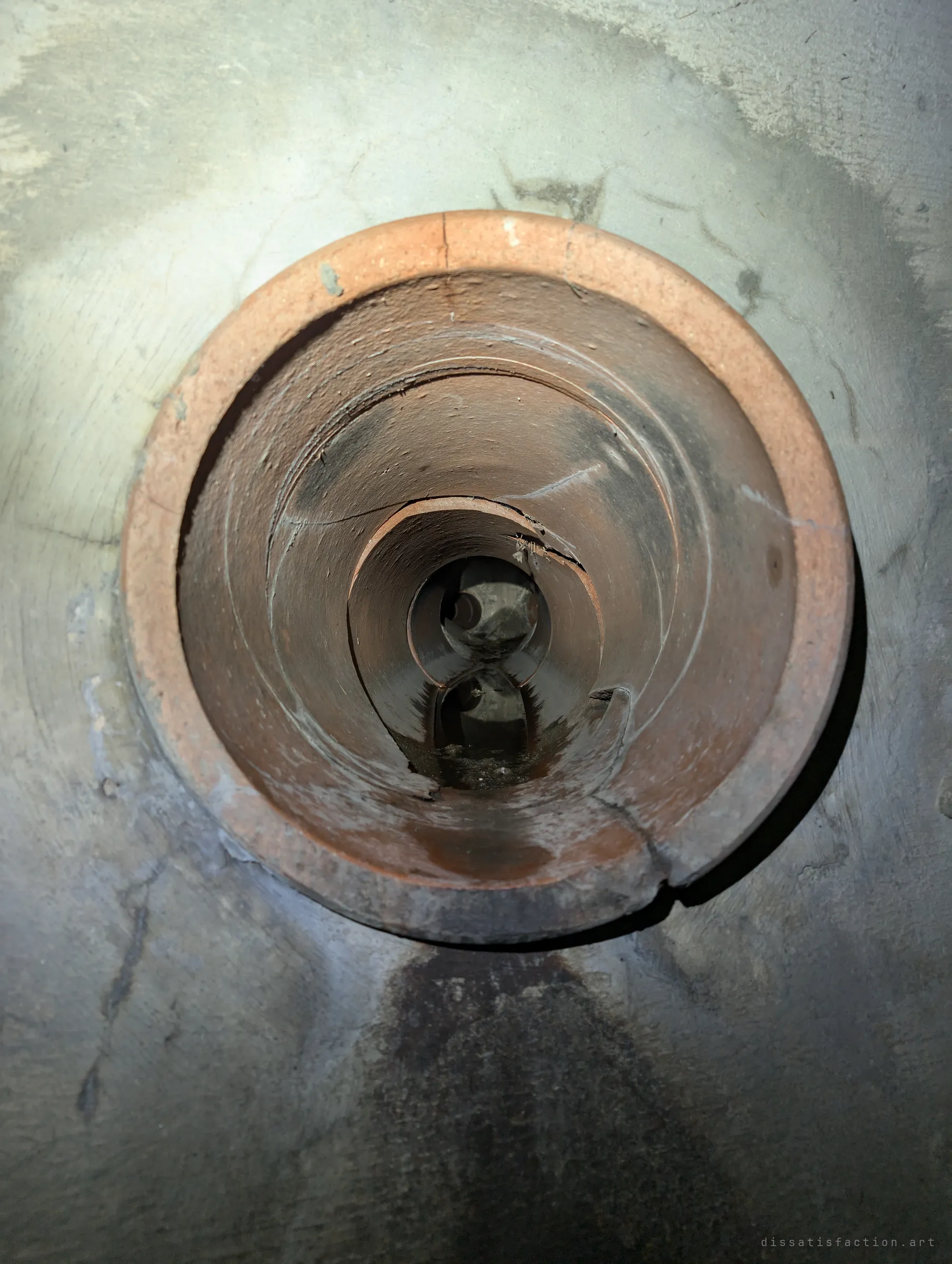 An old clay lateral pipe set into the concrete wall, its cracked terracotta rings telescoping back to a small dark opening.