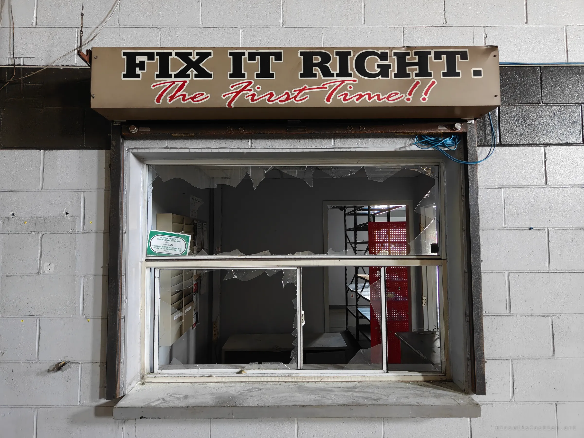 A service-counter window with a smashed pane sits under a worn 'Fix it right. The first time!!' sign, with empty shelving and a red pegboard visible inside.