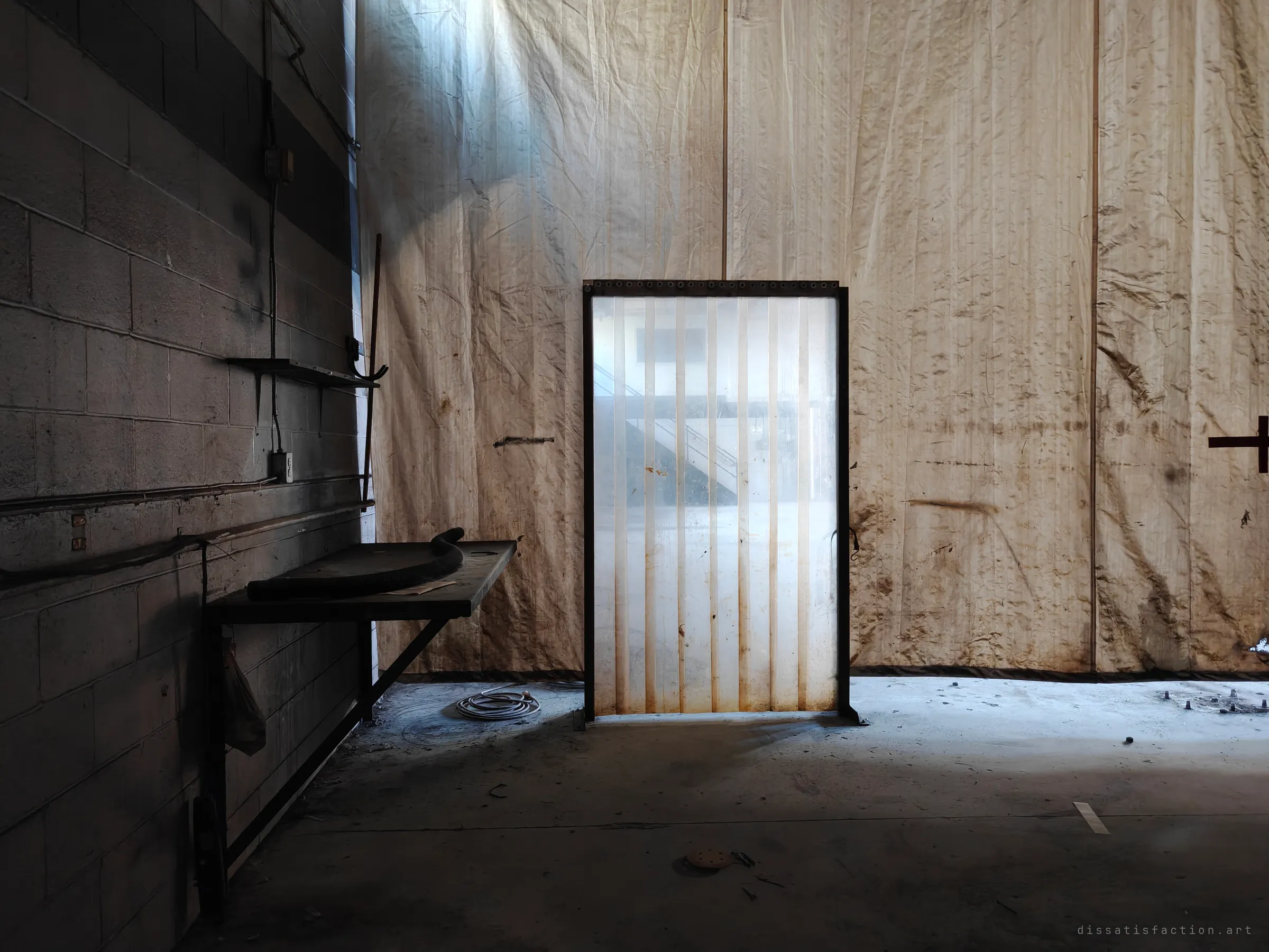 A stained fabric partition hangs across a dim workshop, with a small clear-strip door frame in the middle glowing with light and a bracketed bench against the block wall on the left.