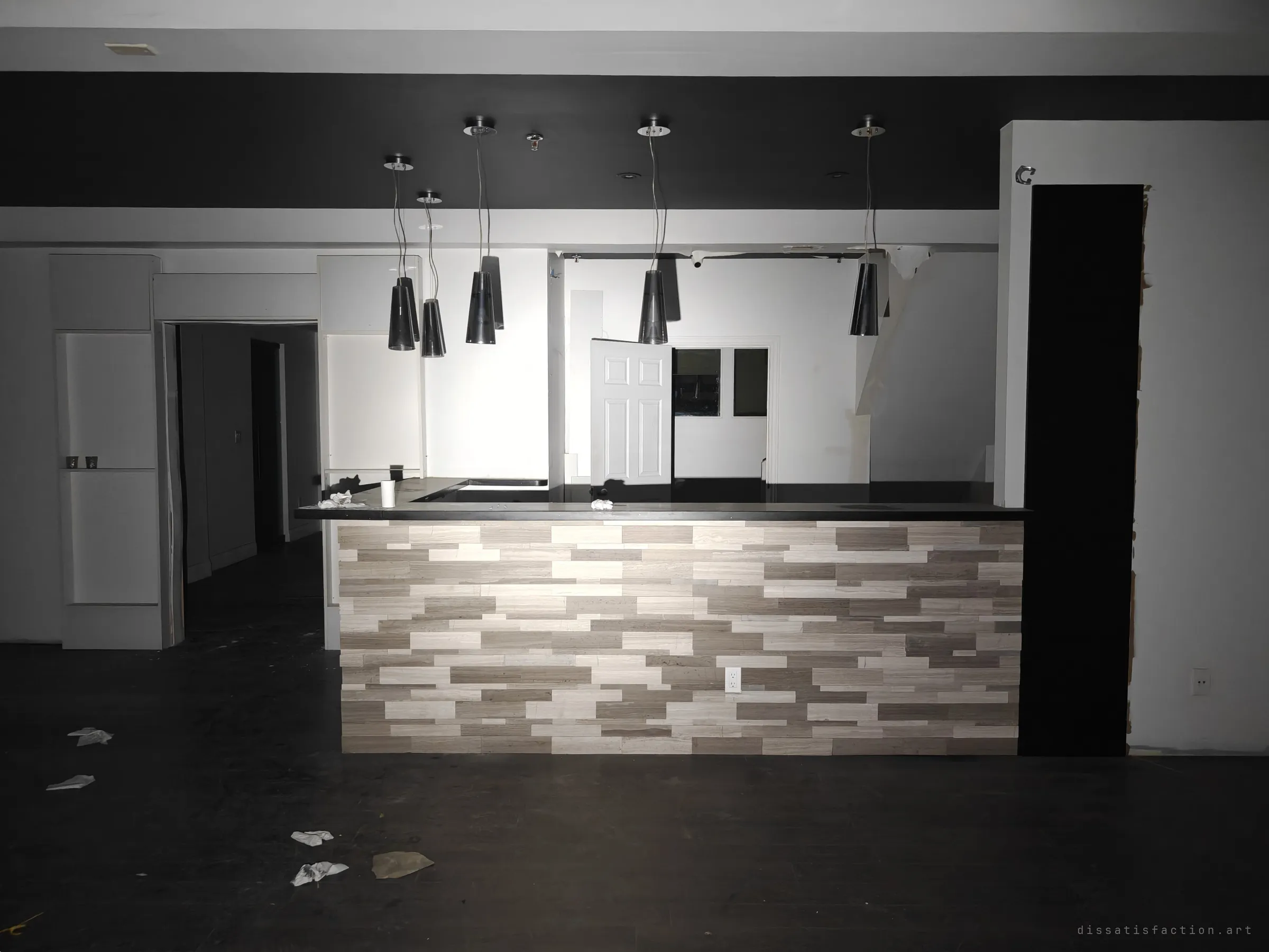 A reception counter faced in striped stone tile under hanging pendant lights, the back rooms open and stripped. The polished fit-out survives while everything around it empties.
