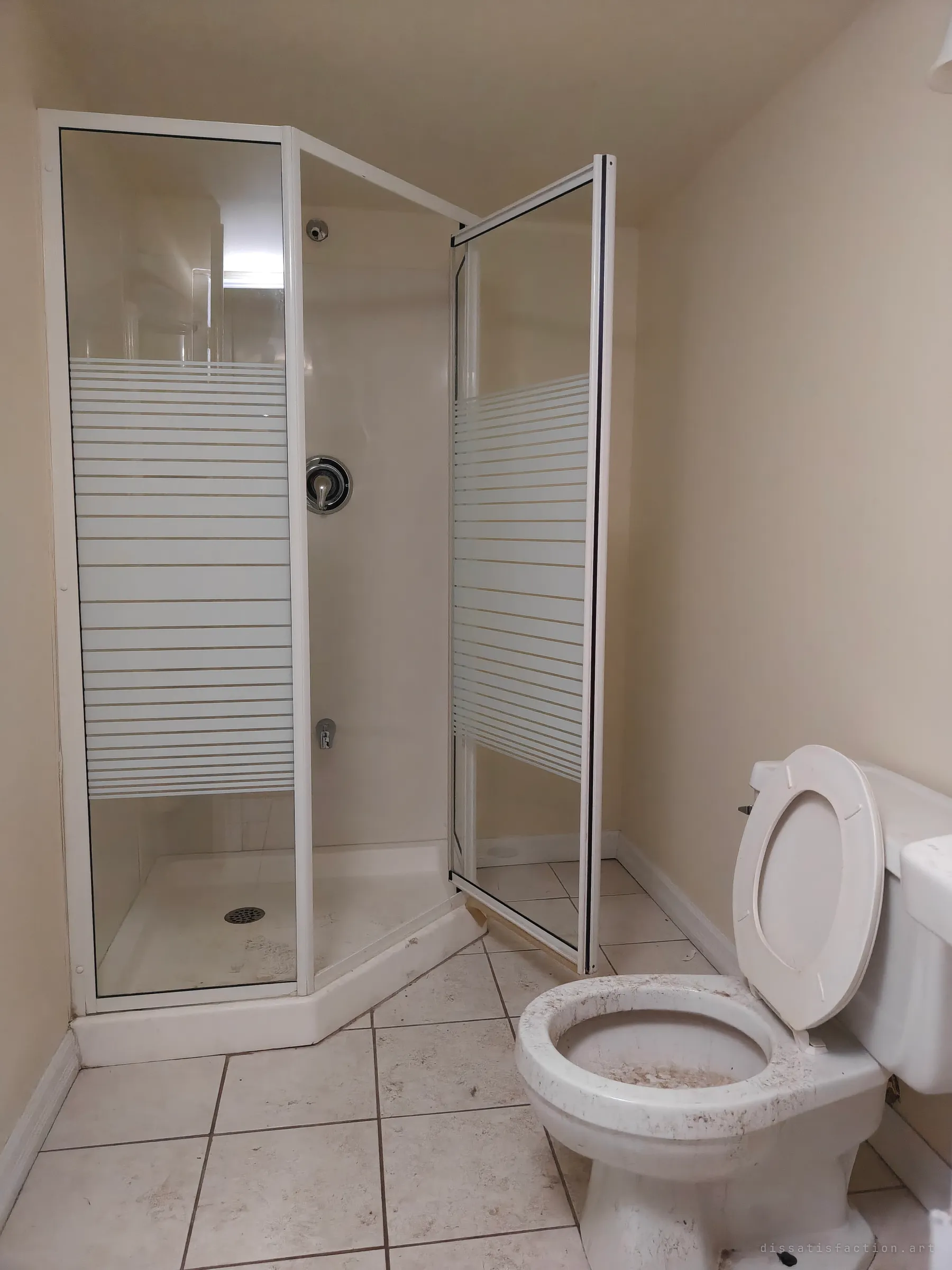A small beige bathroom with a corner shower stall behind striped frosted glass, its door hanging open, beside a grimy, dust-streaked toilet. The mundane fixtures left behind show how recently the space was in daily use.