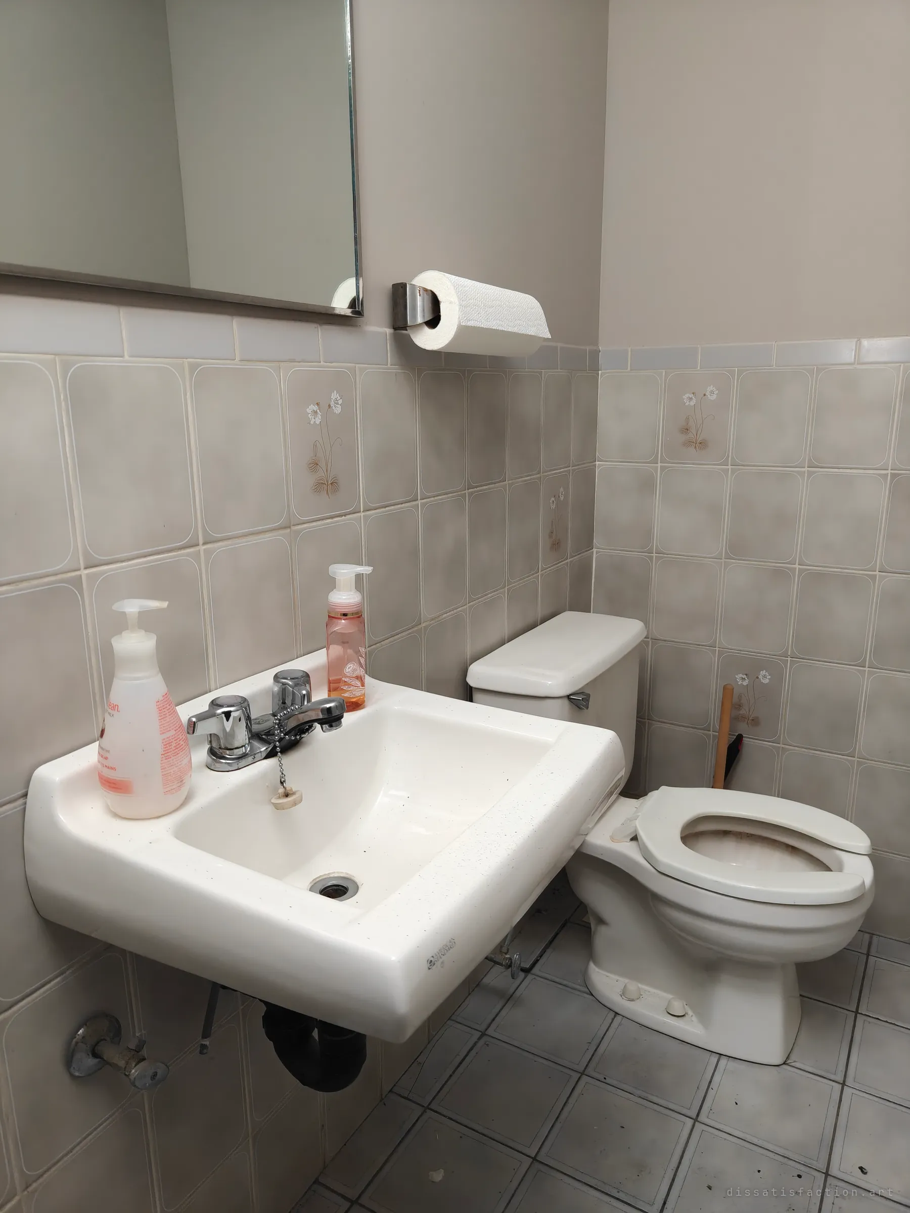A tiled staff washroom with a wall-mounted sink, half-used soap bottles and a paper towel roll still in place next to the toilet. The leftover supplies make the abandonment feel abrupt.