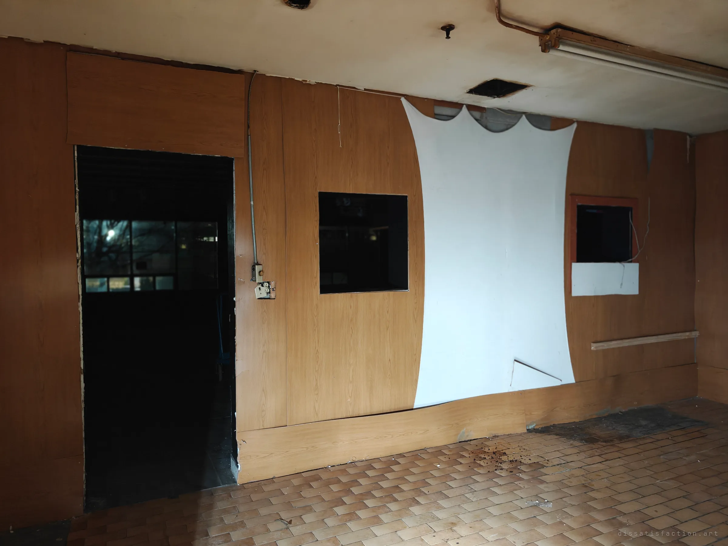 A wood-panelled back room with a sagging white fabric sheet, cut-out pass-through windows and a dark doorway. A moonlit window glows through the far room.