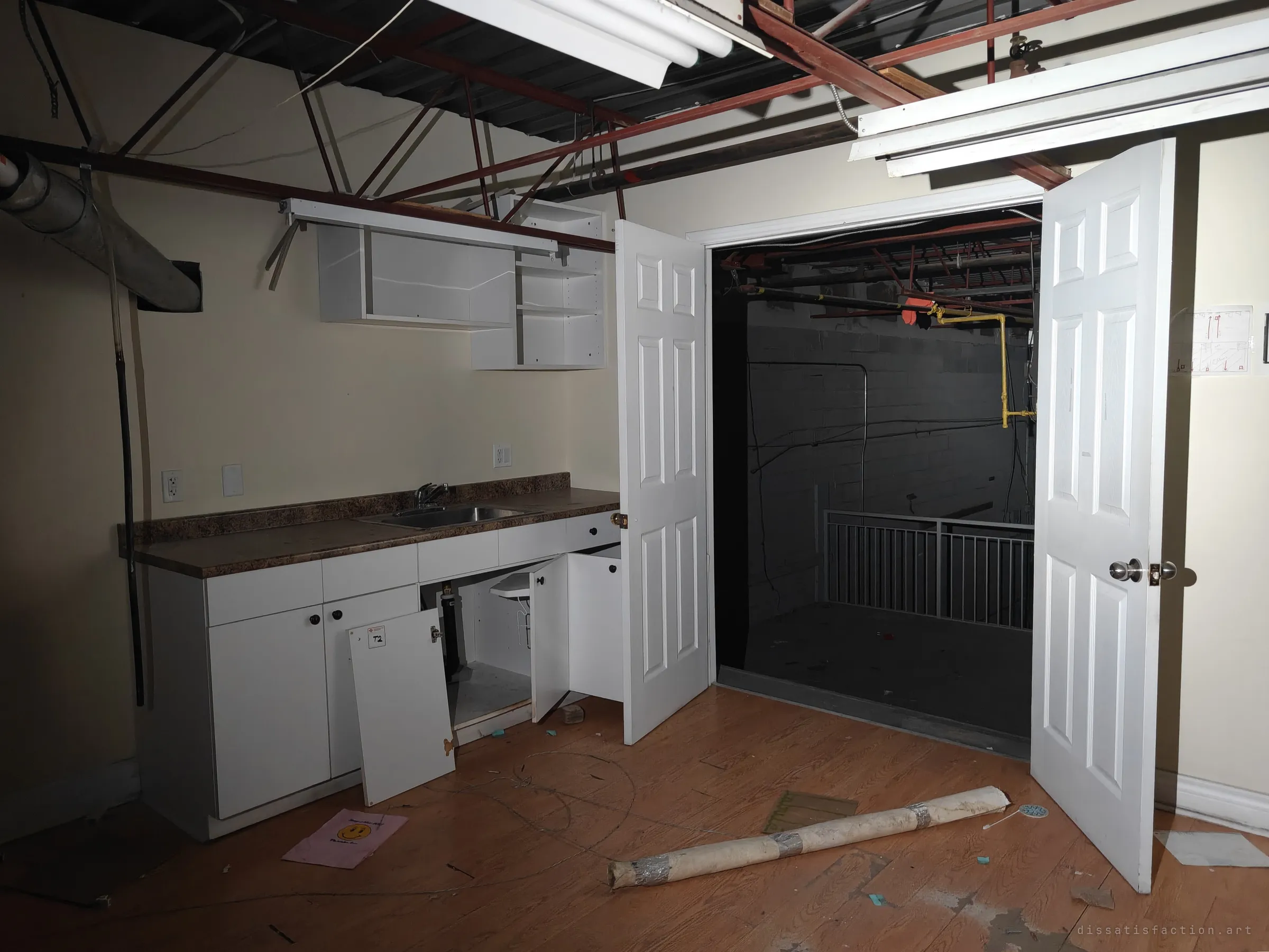 A small upstairs kitchenette with its cabinet doors torn off, double doors opening onto the dark mezzanine. A hand-drawn fire exit plan is still taped by the door.