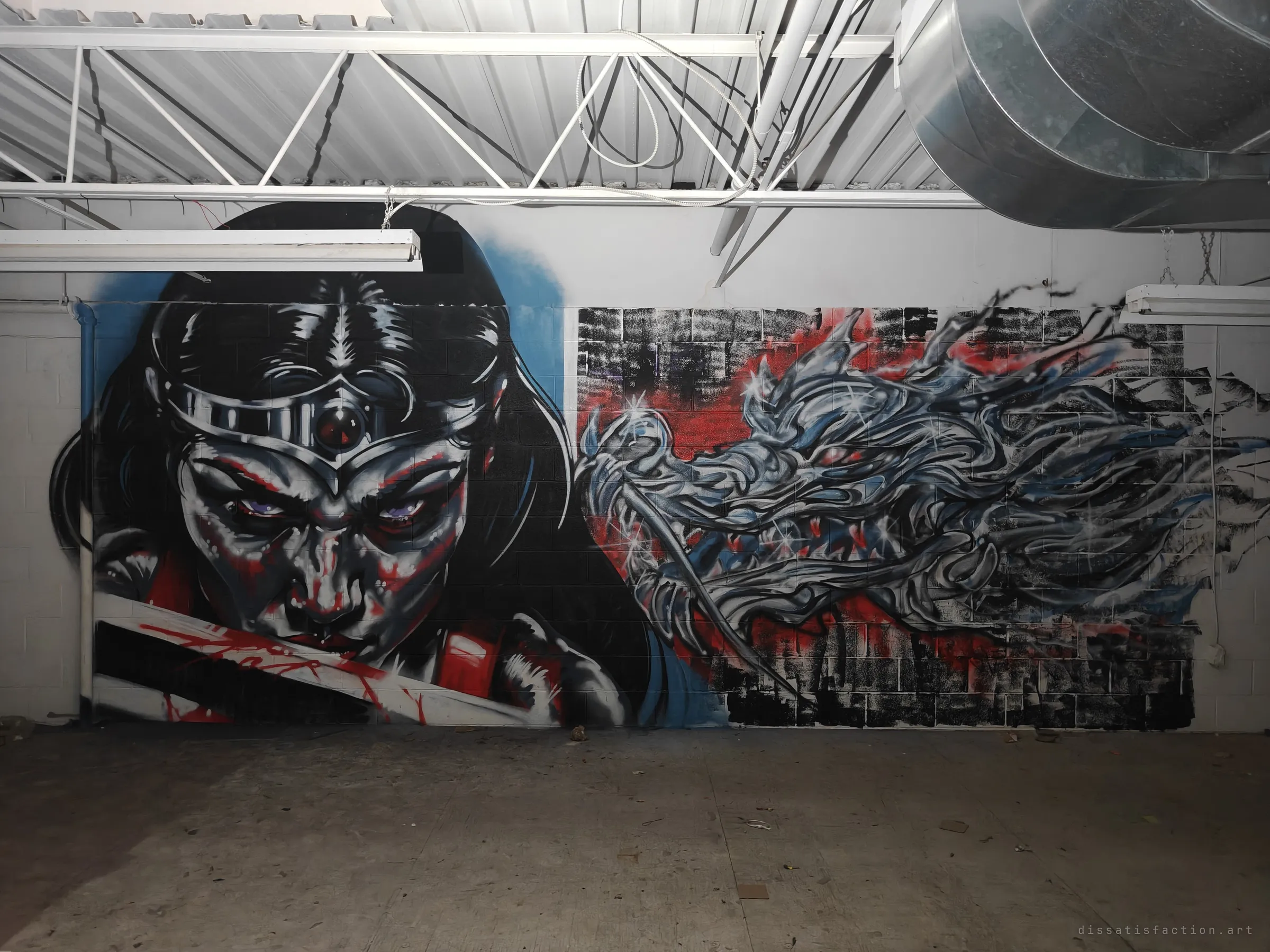 A large mural of a masked warrior woman and a silver dragon painted across the warehouse block wall. It is the most striking thing left in the empty unit.