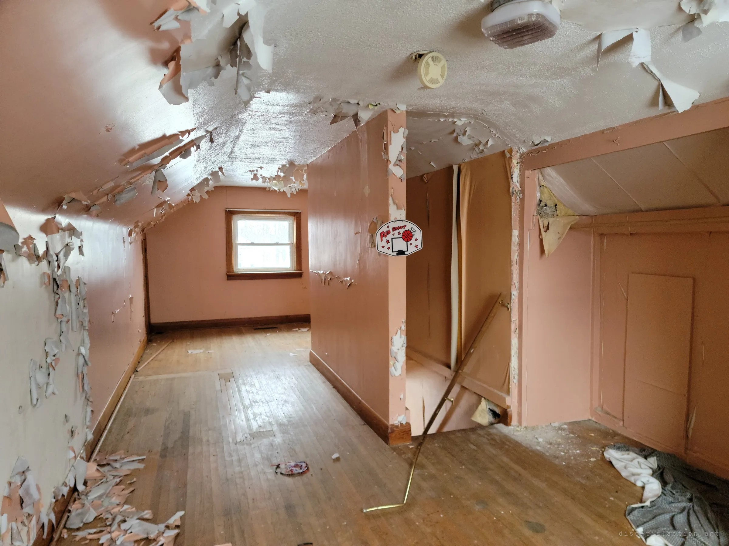 An attic floor with pink walls and ceiling paint peeling away in curled sheets, a toy basketball backboard hanging on a post by the stairwell. A child's room slowly shedding its skin.