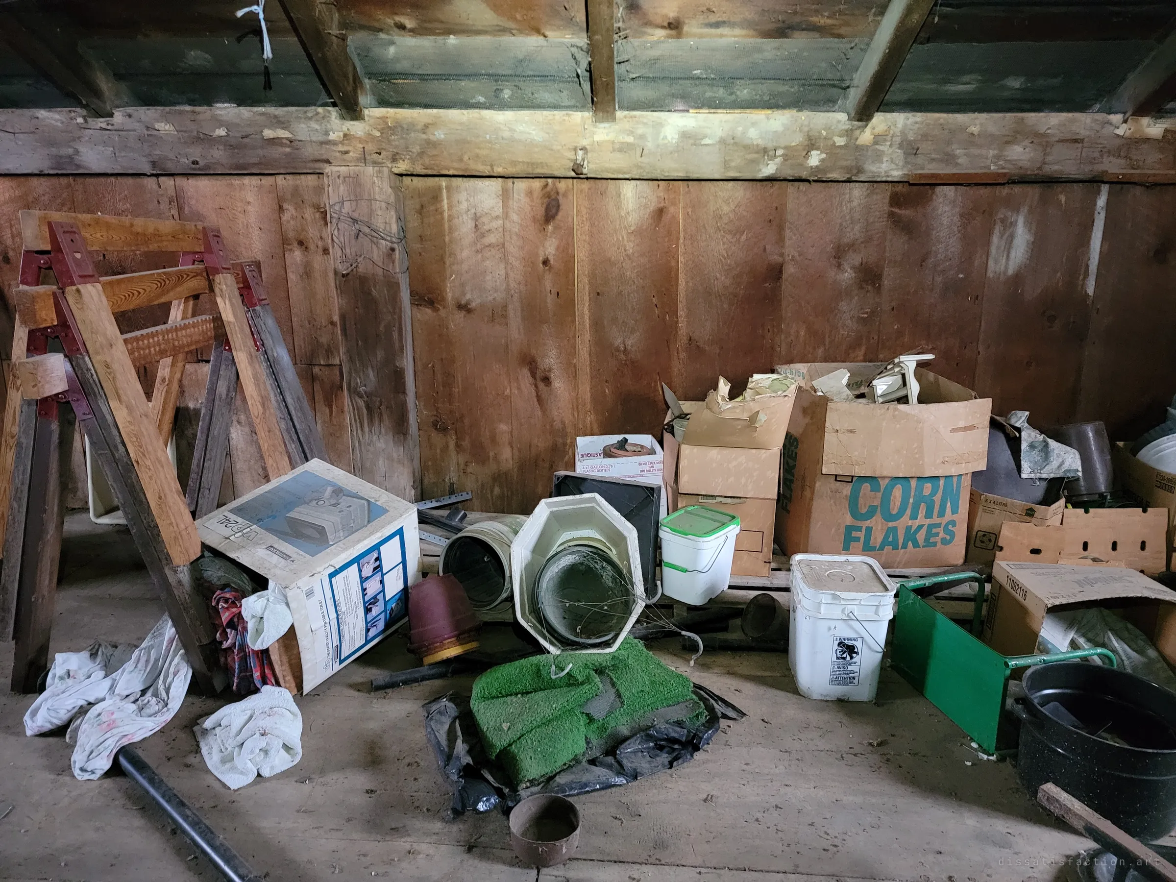 Stacked cardboard boxes, buckets, sawhorses and a scrap of artificial turf are piled against the rough plank wall of the attic. Years of stored odds and ends left exactly where they were set down.