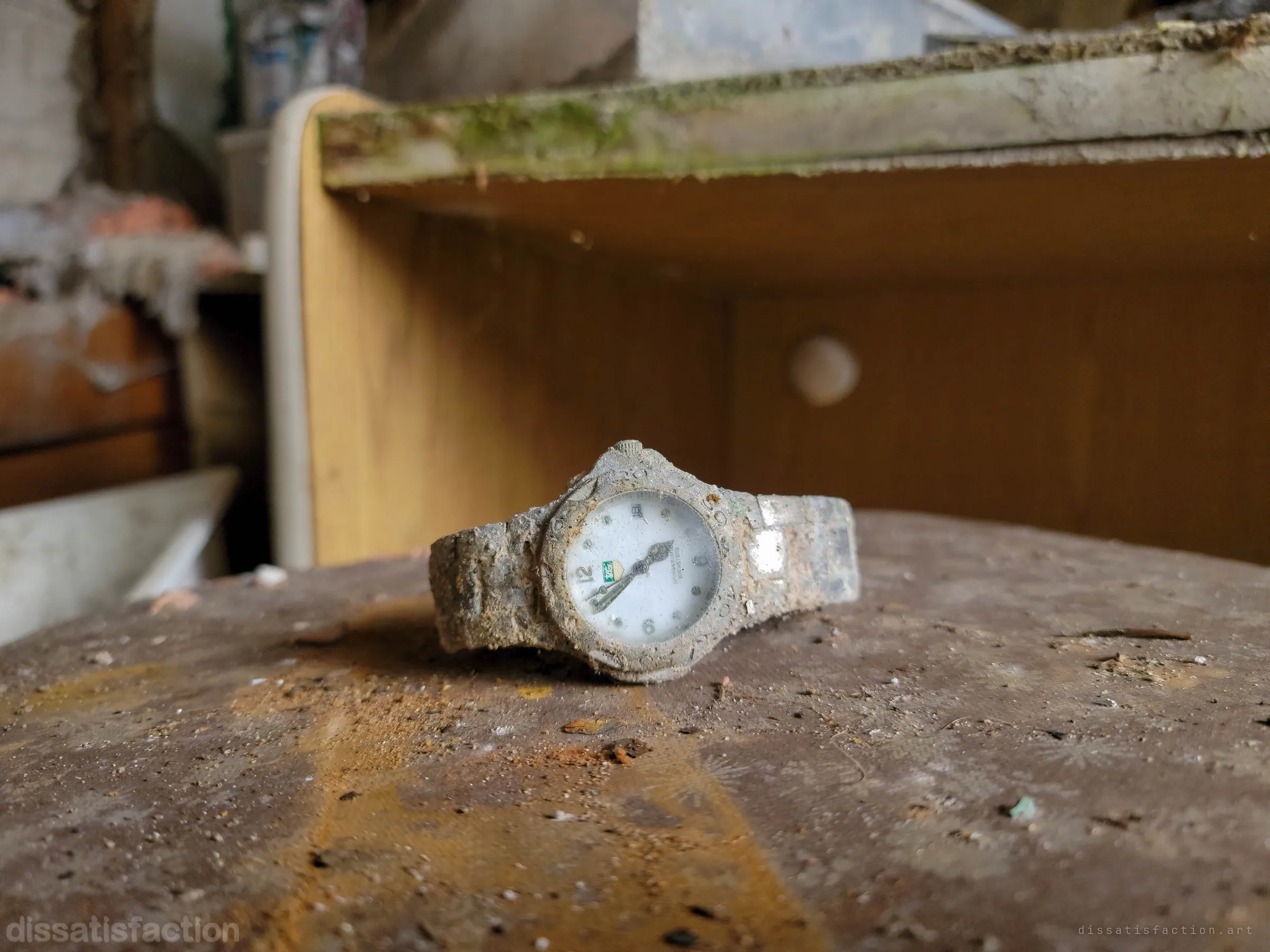 Close-up of a dirt-crusted wristwatch lying on a stained wooden surface, the rest of the room blurred behind it. A small personal object frozen in the decay.