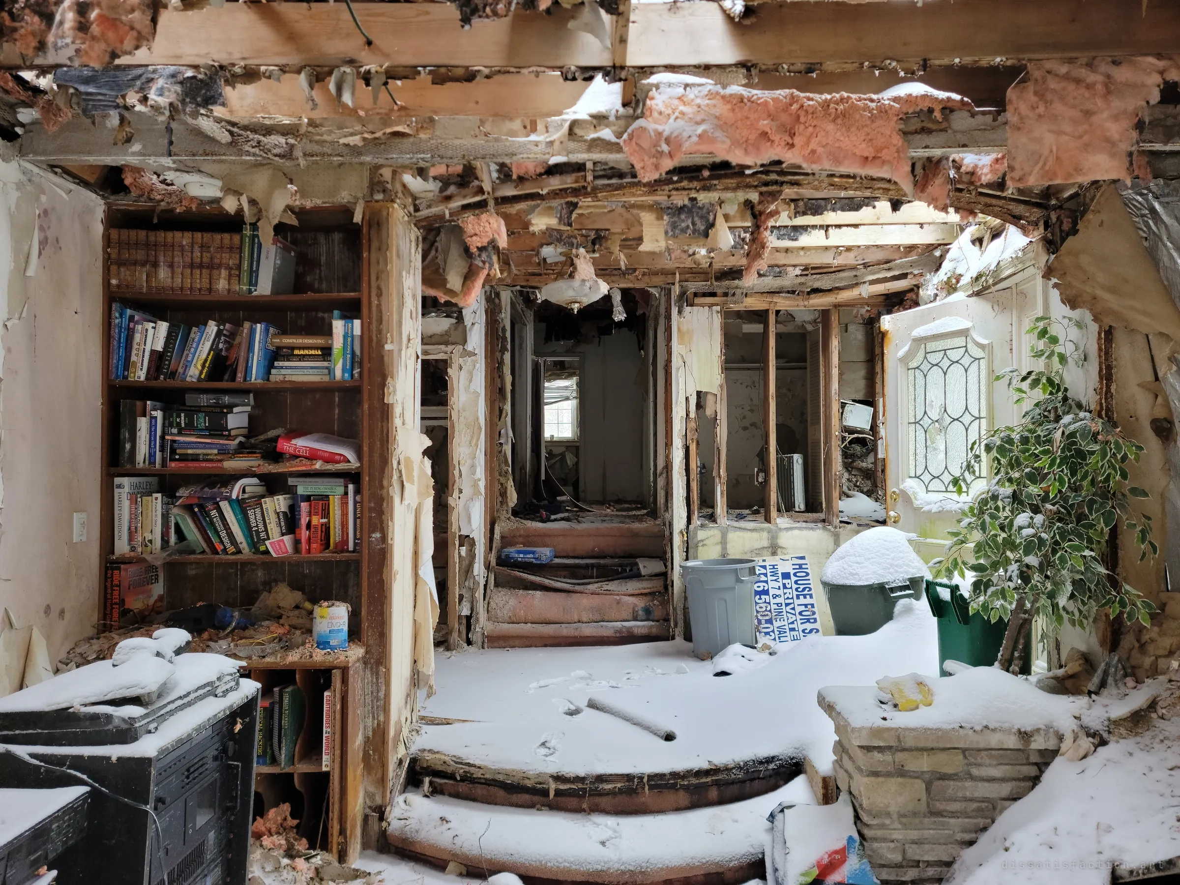 A sunken foyer with steps up to a stripped hallway, a bookshelf on the left and a snow-dusted plant by the leaded-glass front door. An old sale sign leans between the bins, never answered.