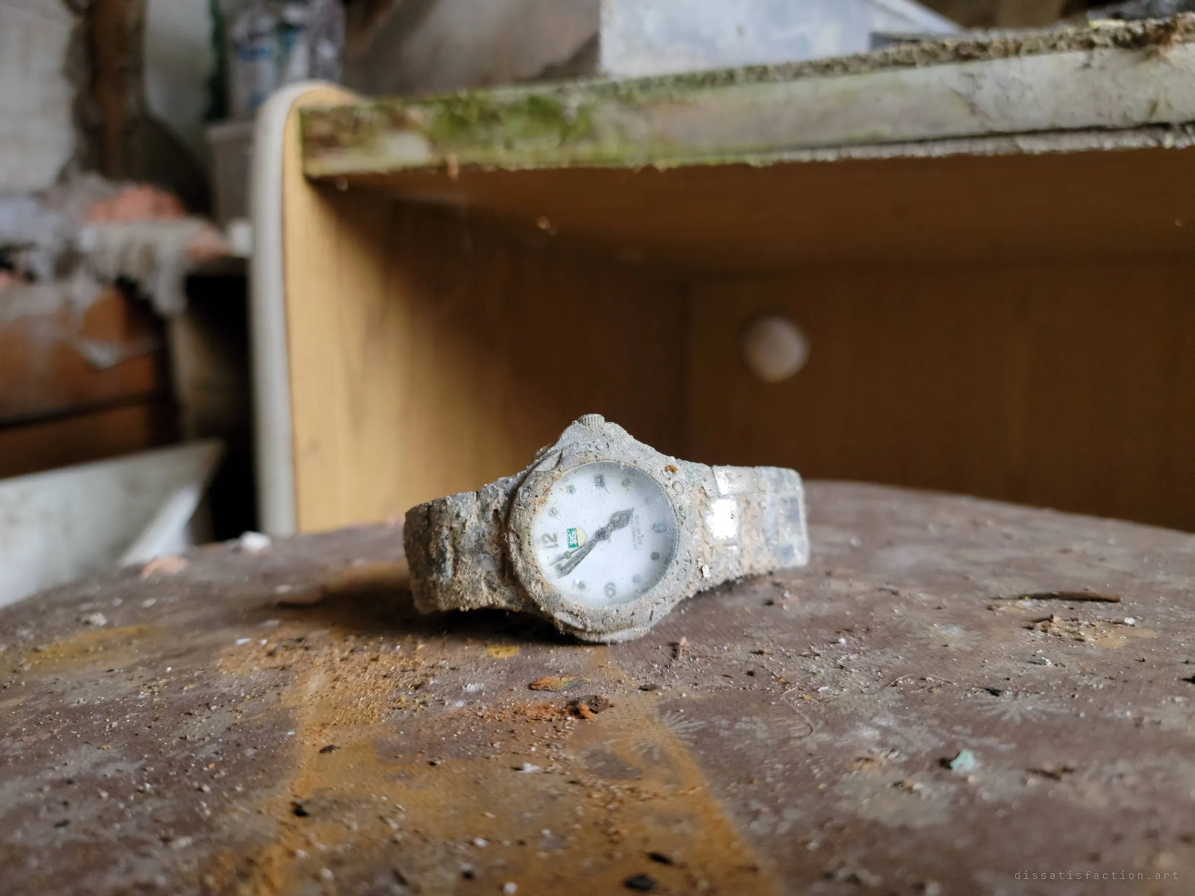 Close-up of the same wristwatch, its dial crusted in grime, lying on a stained round tabletop before a mossy shelf. Its stopped hands feel like a marker of when the house was left.