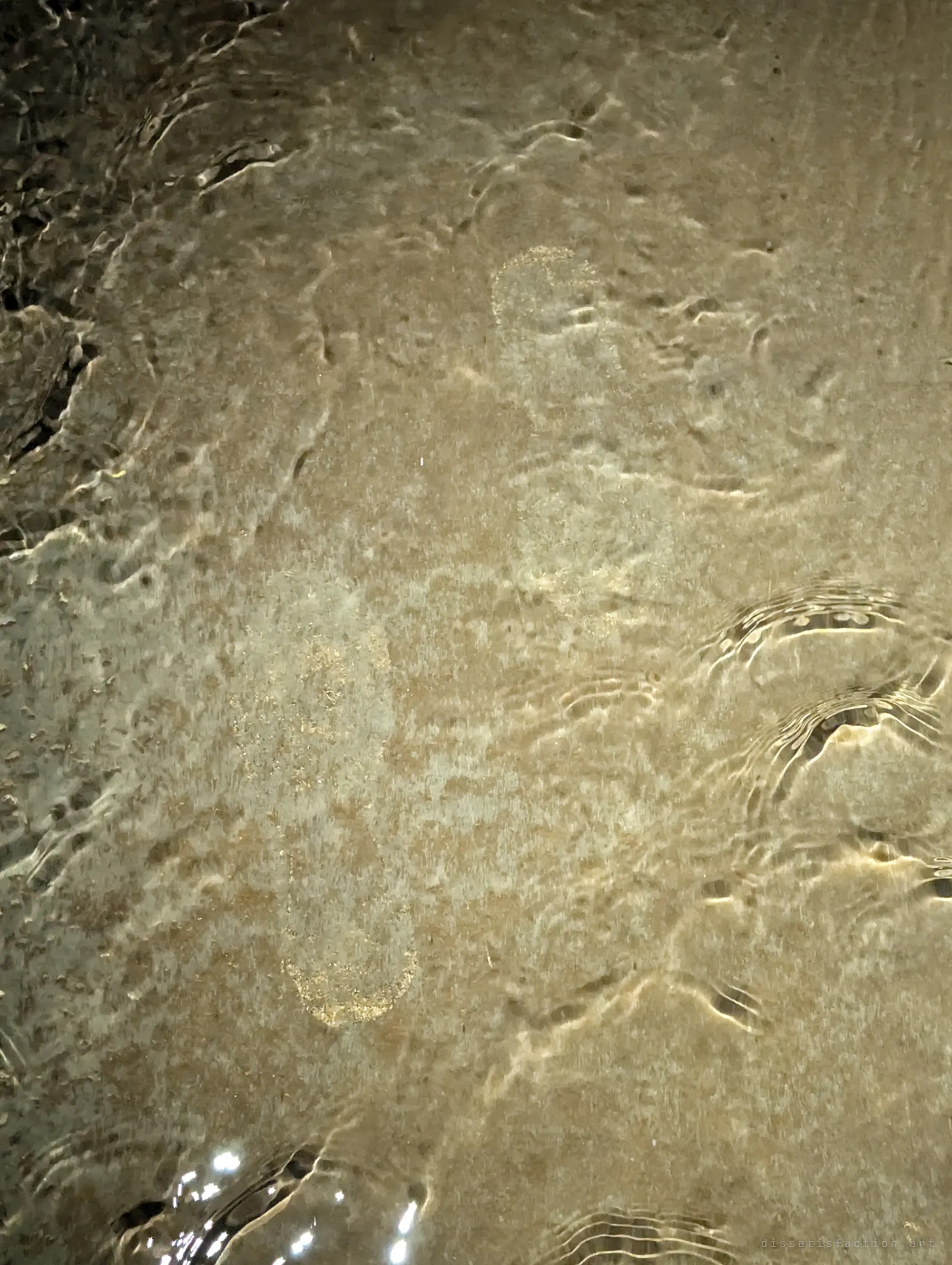 Faint footprints pressed into silt show through a thin sheet of rippling water on the culvert floor, a trace of someone who came through before.