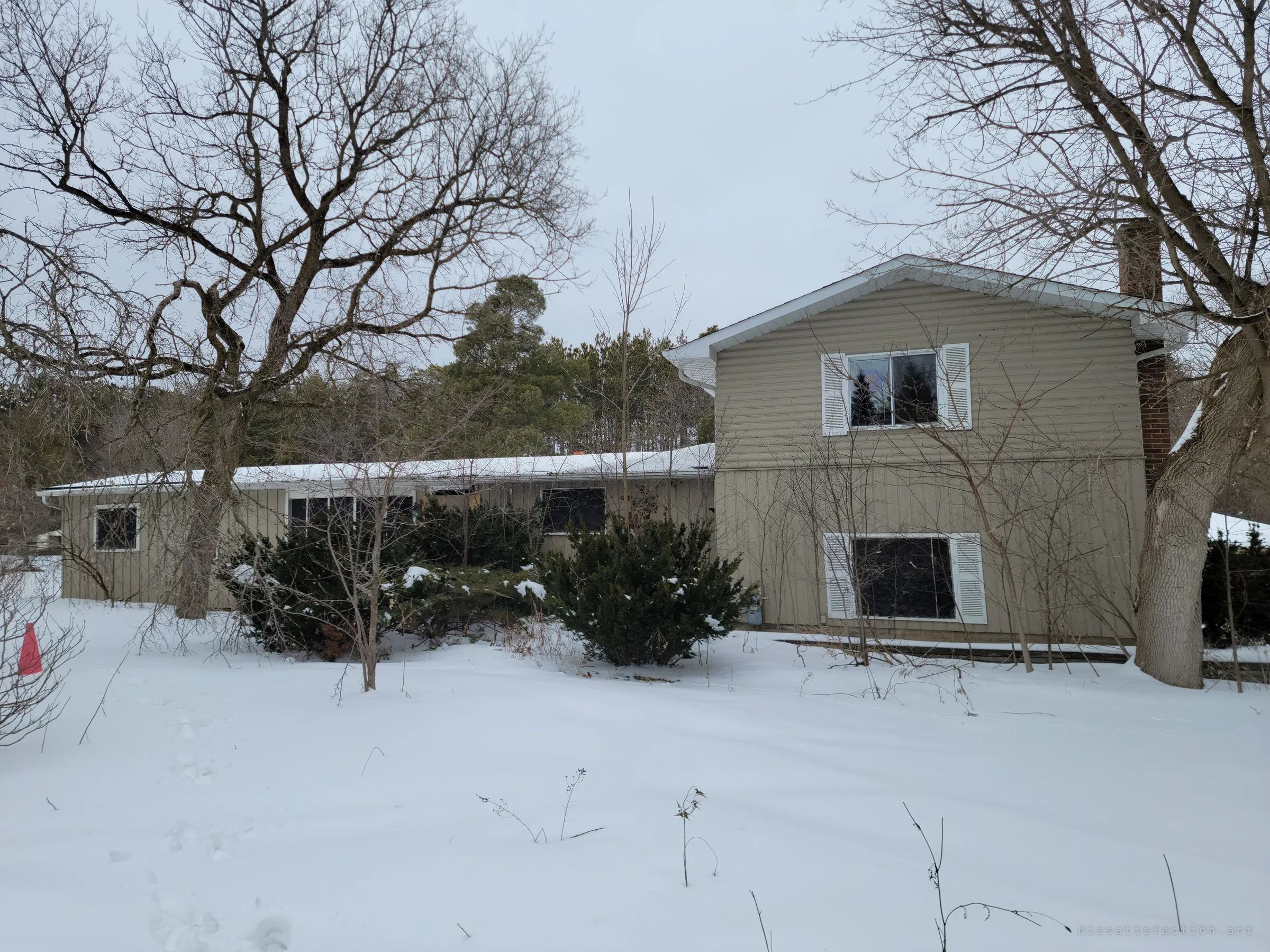 A snow-covered split-level house with beige siding and shuttered windows sits behind bare winter trees. It sets the scene: the home is empty and the yard untouched except for footprints.