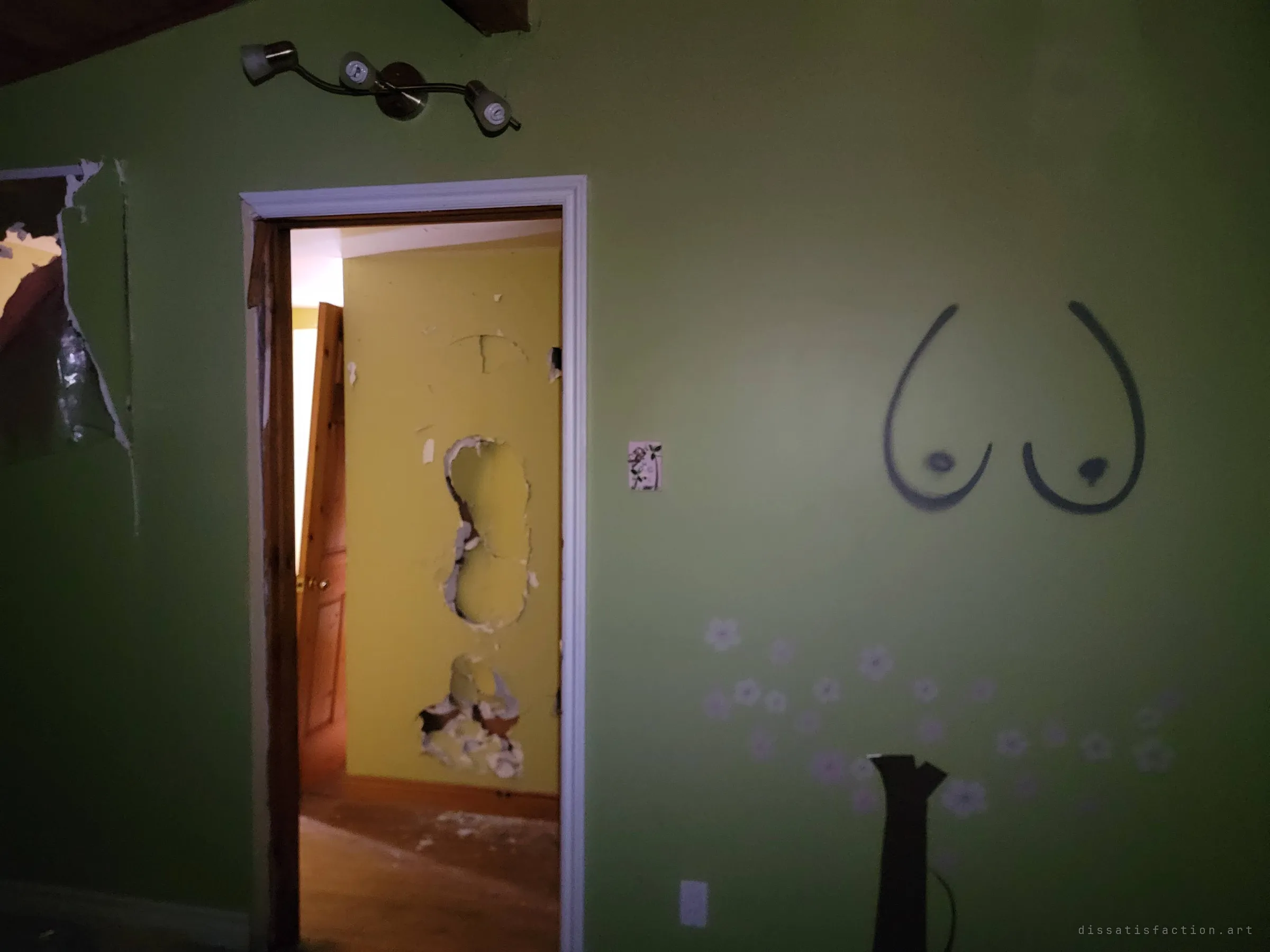 A lime-green bedroom wall with spray-painted graffiti and faded flower decals beside a doorway into a yellow hall with torn-out drywall. The nursery paint and later vandalism sit side by side.