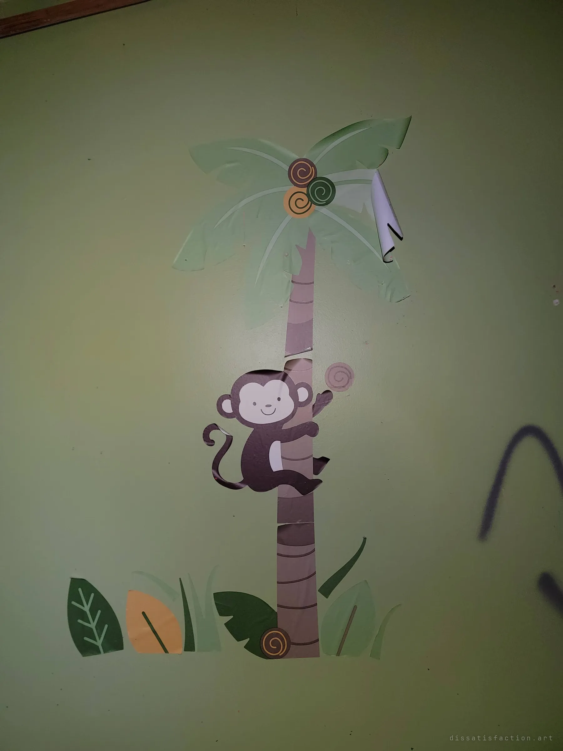 A cartoon monkey decal climbing a palm tree above jungle leaves, with a stroke of black spray paint creeping in from the right. Childhood decor meets later graffiti.