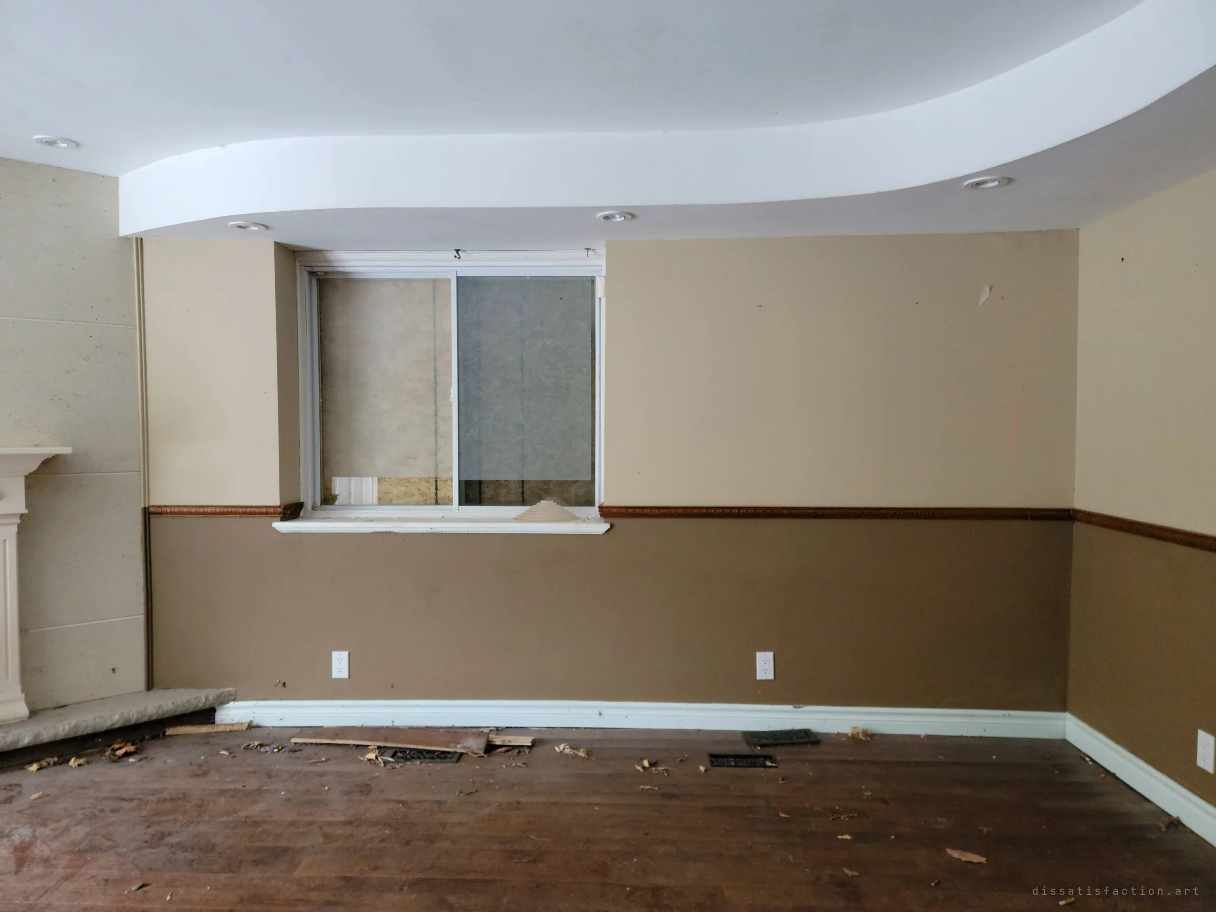 The other side of the same room: a two-tone wall under a curved dropped ceiling, with a small basement window boarded from outside. Clean and quiet, with only leaves and loose vents on the floor.