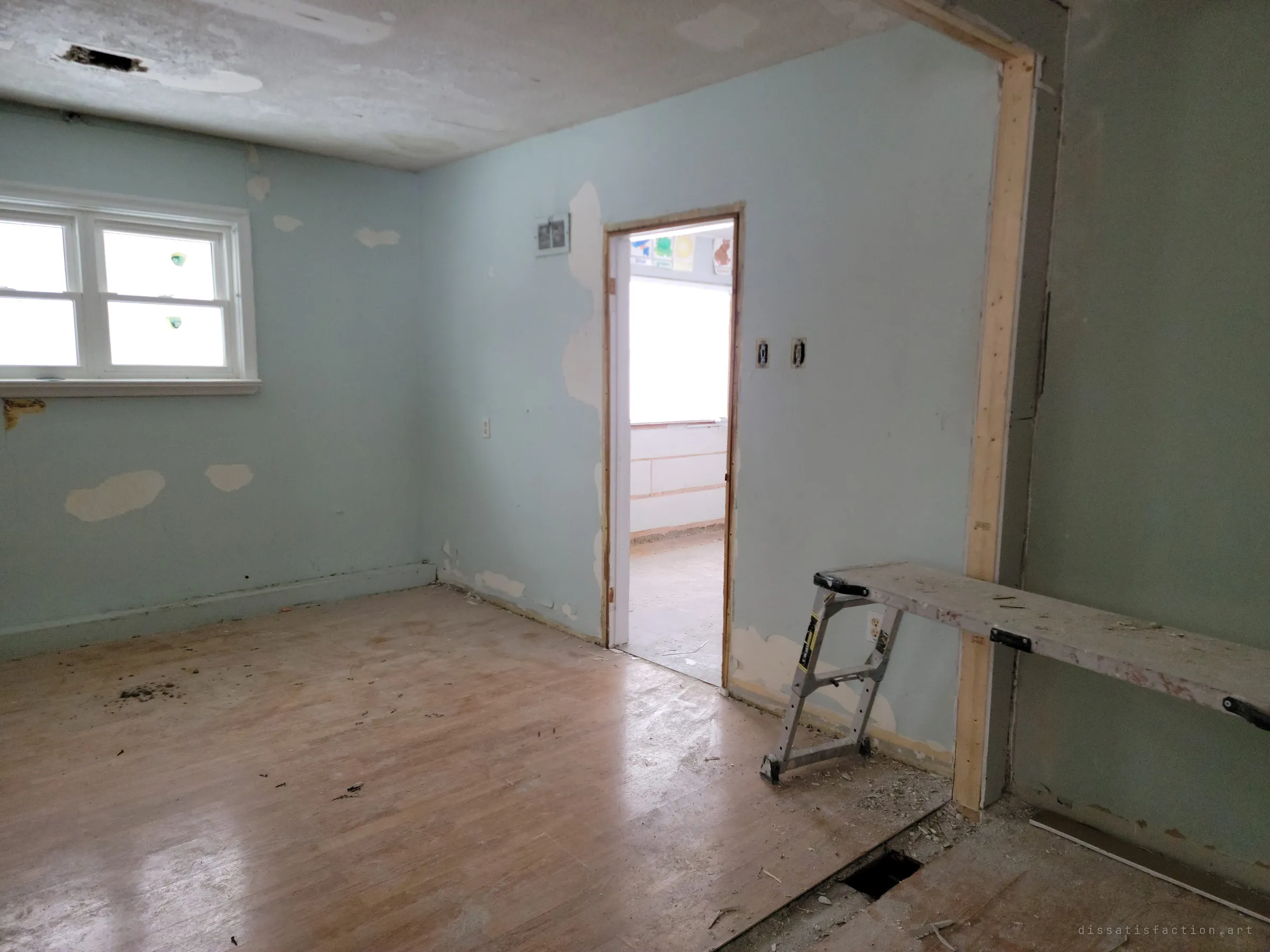 An emptied pale-green room with patched walls, a fresh stud frame and a painter's work platform. The half-finished repairs show the building caught partway through renovation.