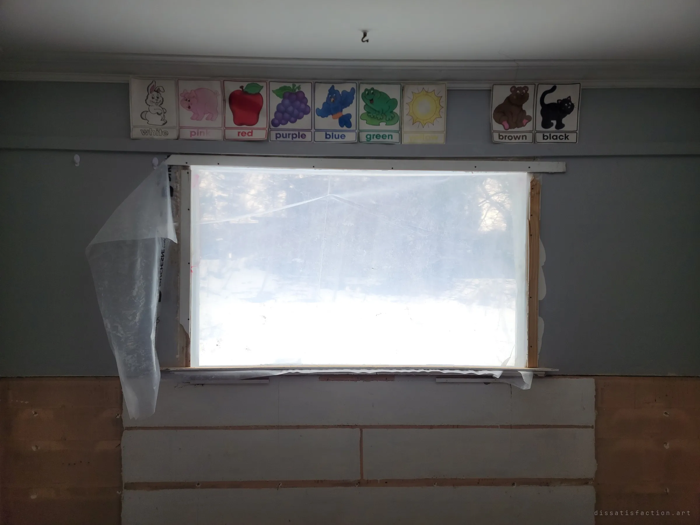 A row of children's colour-word flashcards still lines the wall above a window covered in plastic sheeting. The teaching cards left behind mark this as a former classroom.