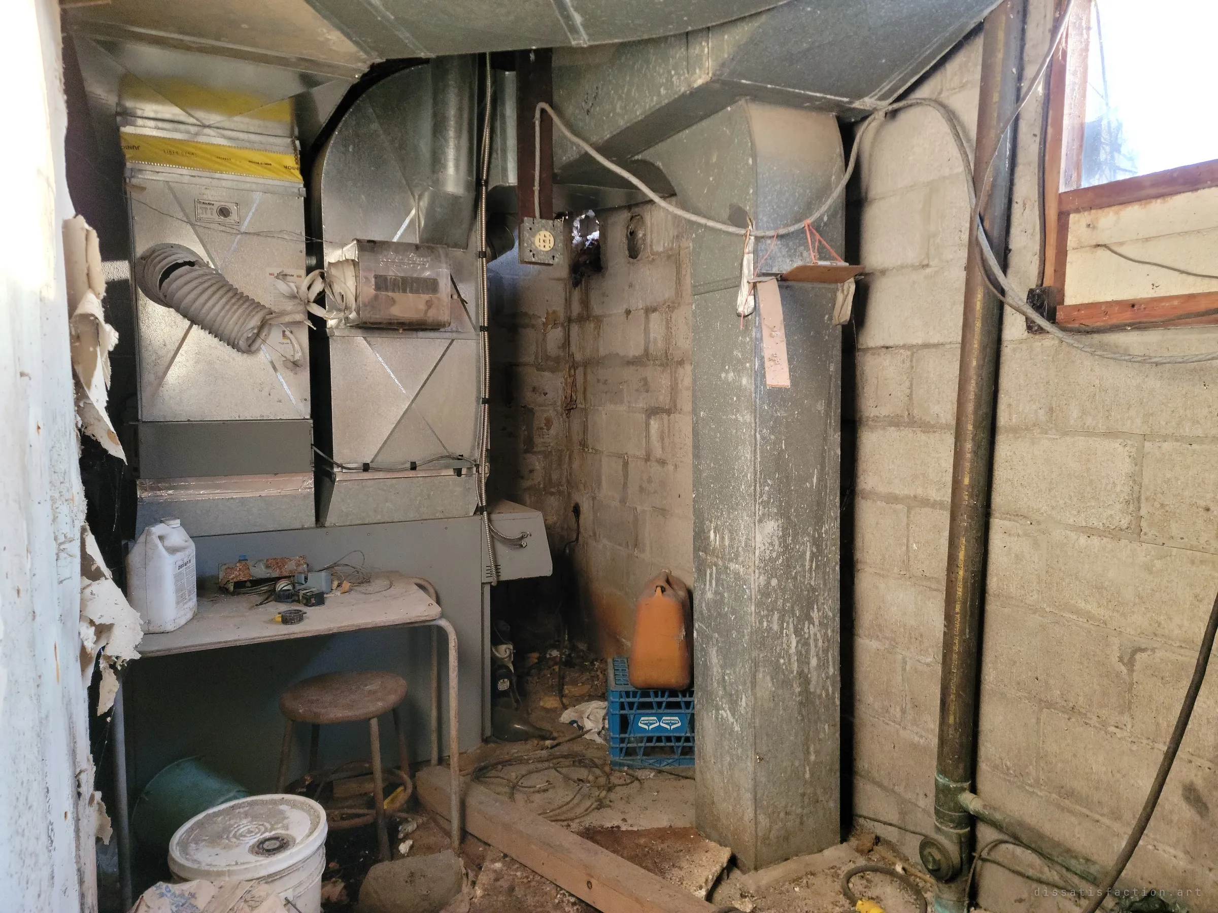 A cramped furnace room of galvanised ducts, a stool and a work table against bare block walls. The house's old heating plant, gutted and abandoned mid-repair.