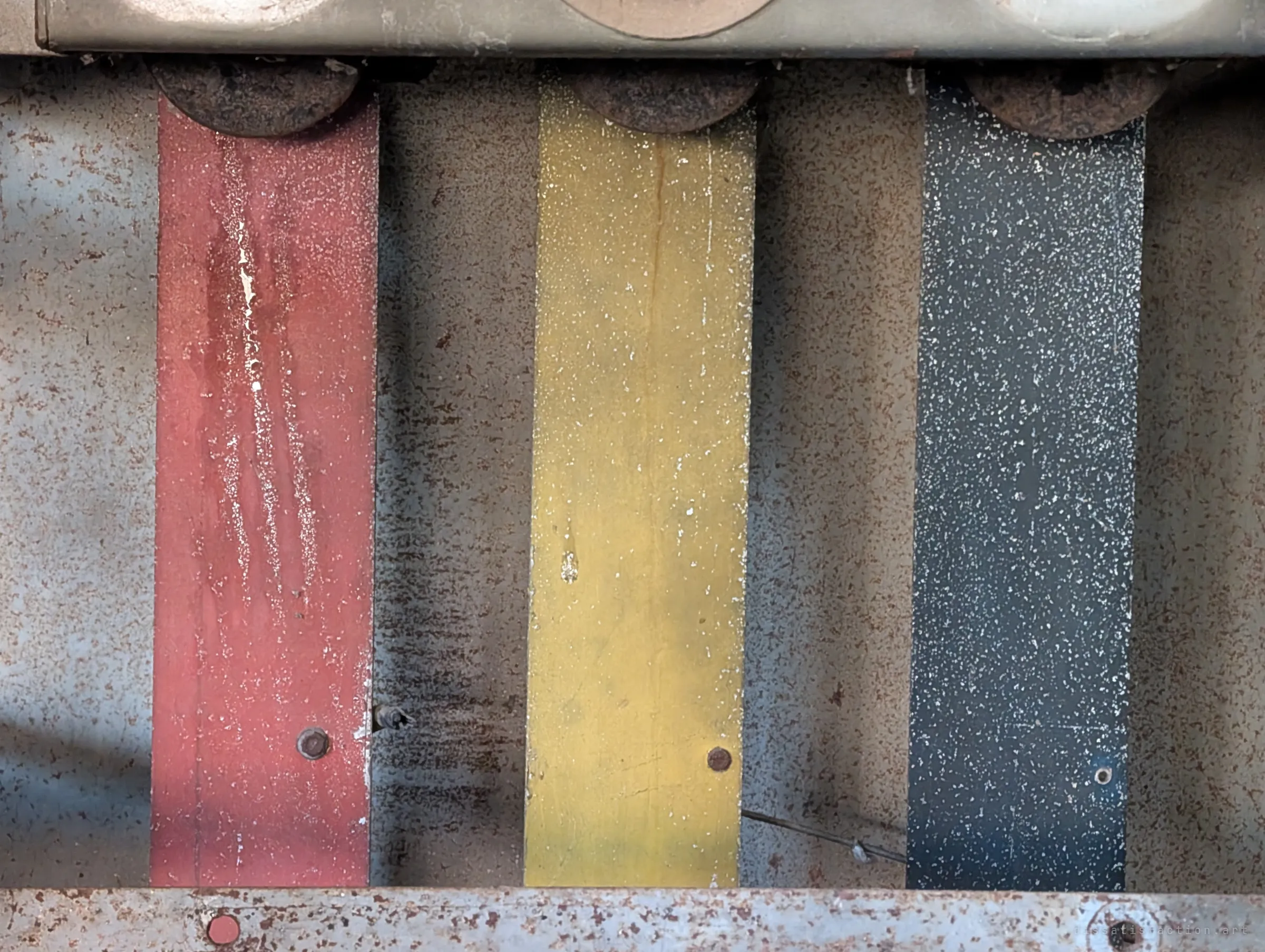 Close-up of three painted busbars in red, yellow and blue against a rust-freckled steel back panel. By chance the phase colours line up like a national tricolour.