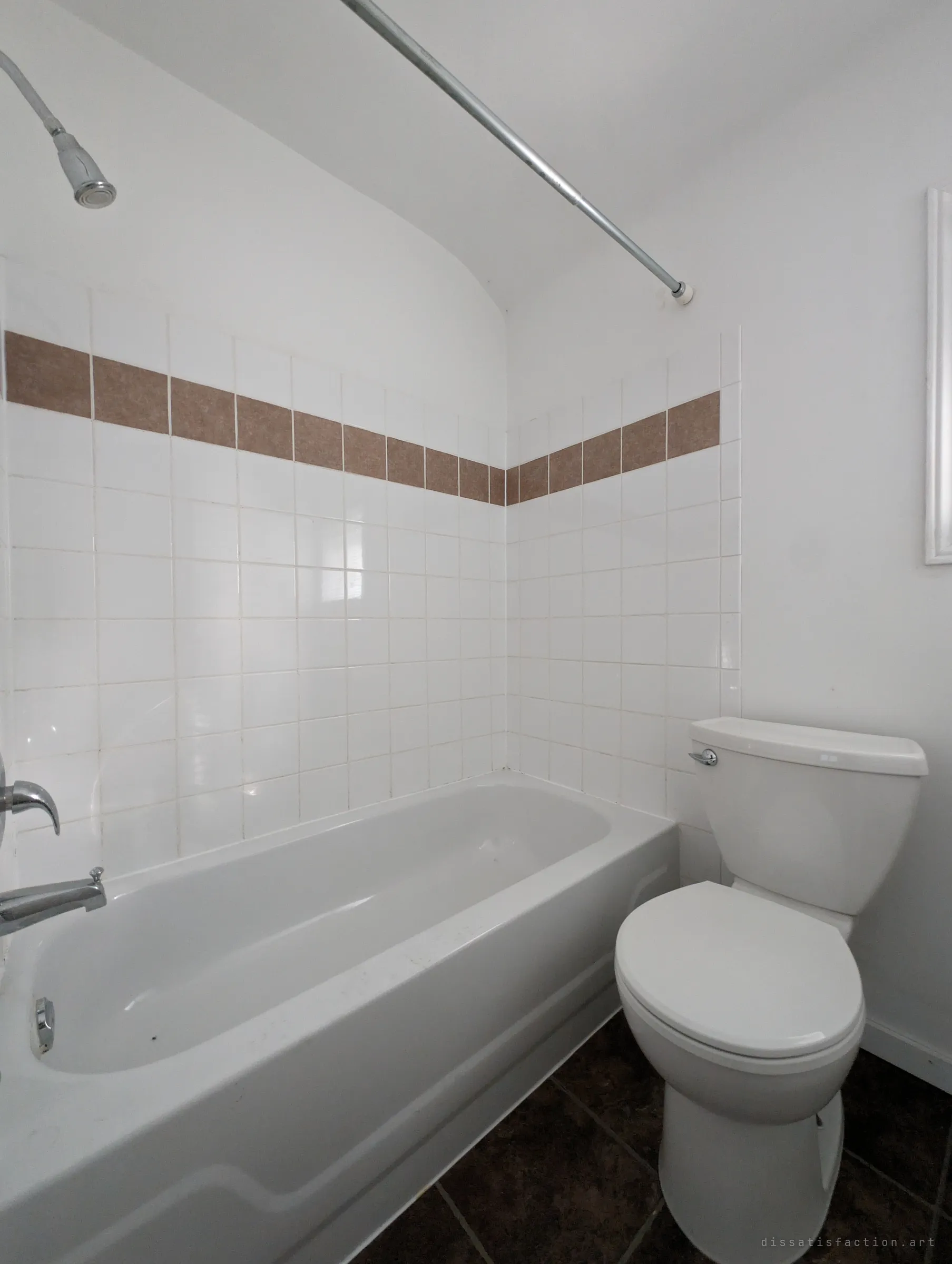 A small white-tiled bathroom under a sloped ceiling, with a single band of brown accent tiles above a clean, empty tub.