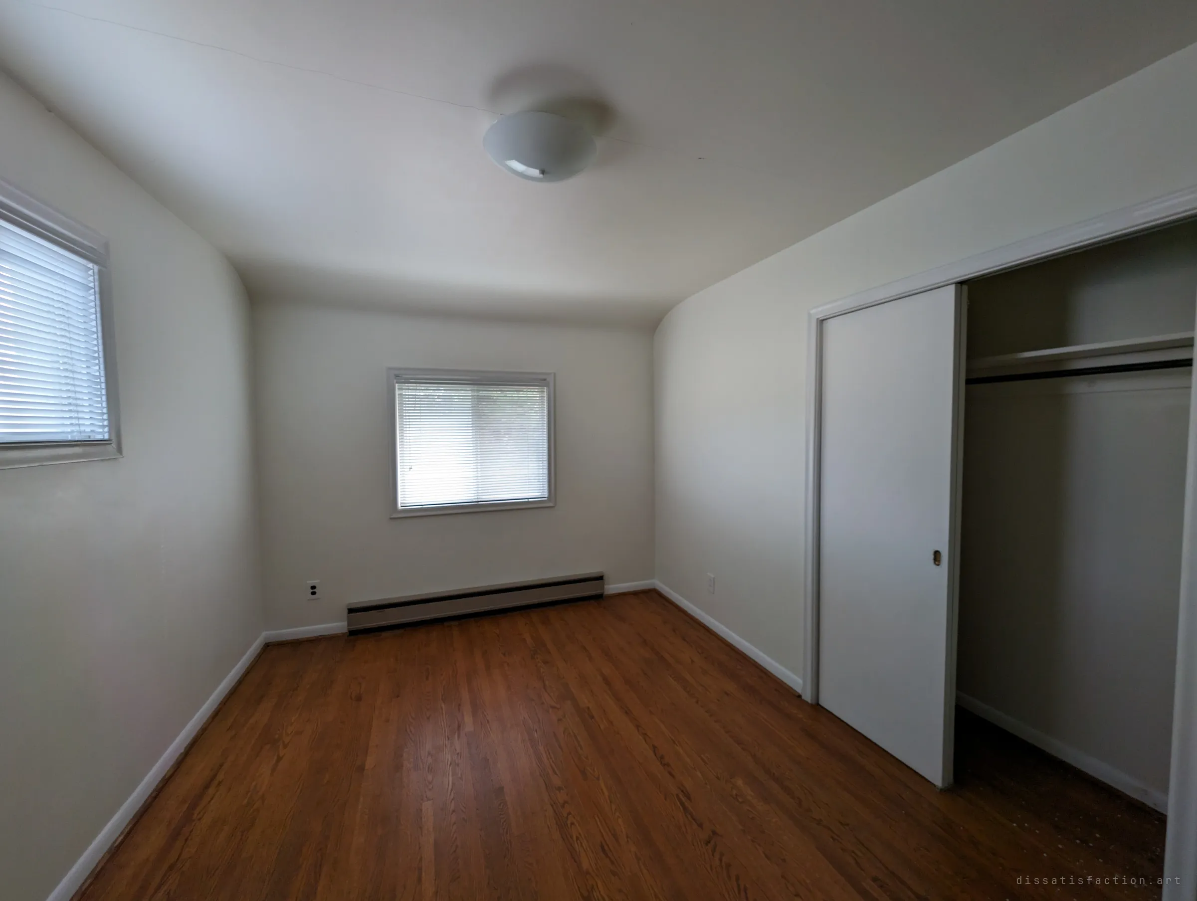 An empty bedroom under the eaves, with curved ceiling edges, hardwood floors and a half-open closet; the house looks cleaned out rather than left behind.