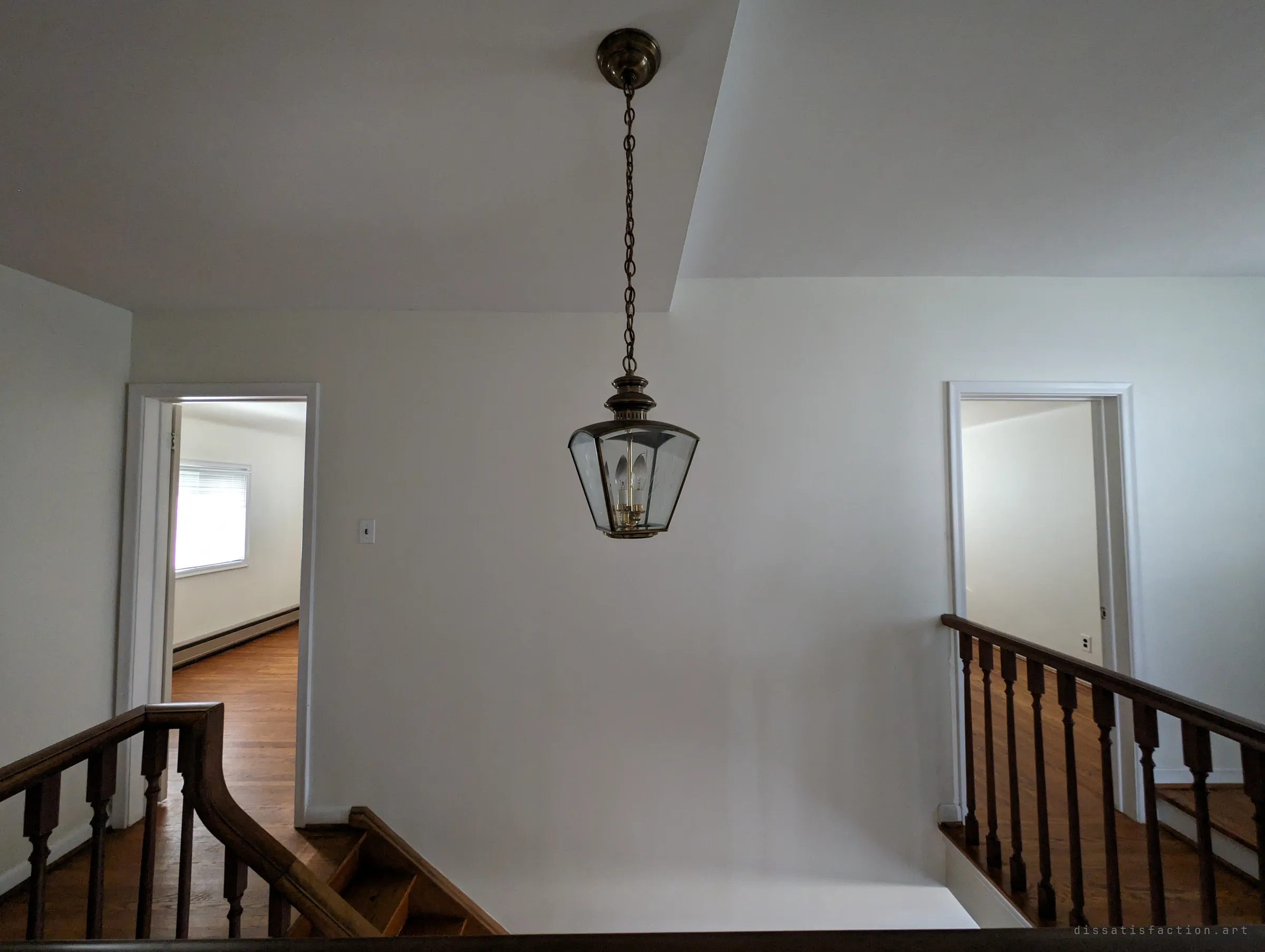 A brass lantern hangs over the upstairs landing between two open bedroom doors, wooden banisters framing the stairwell below.