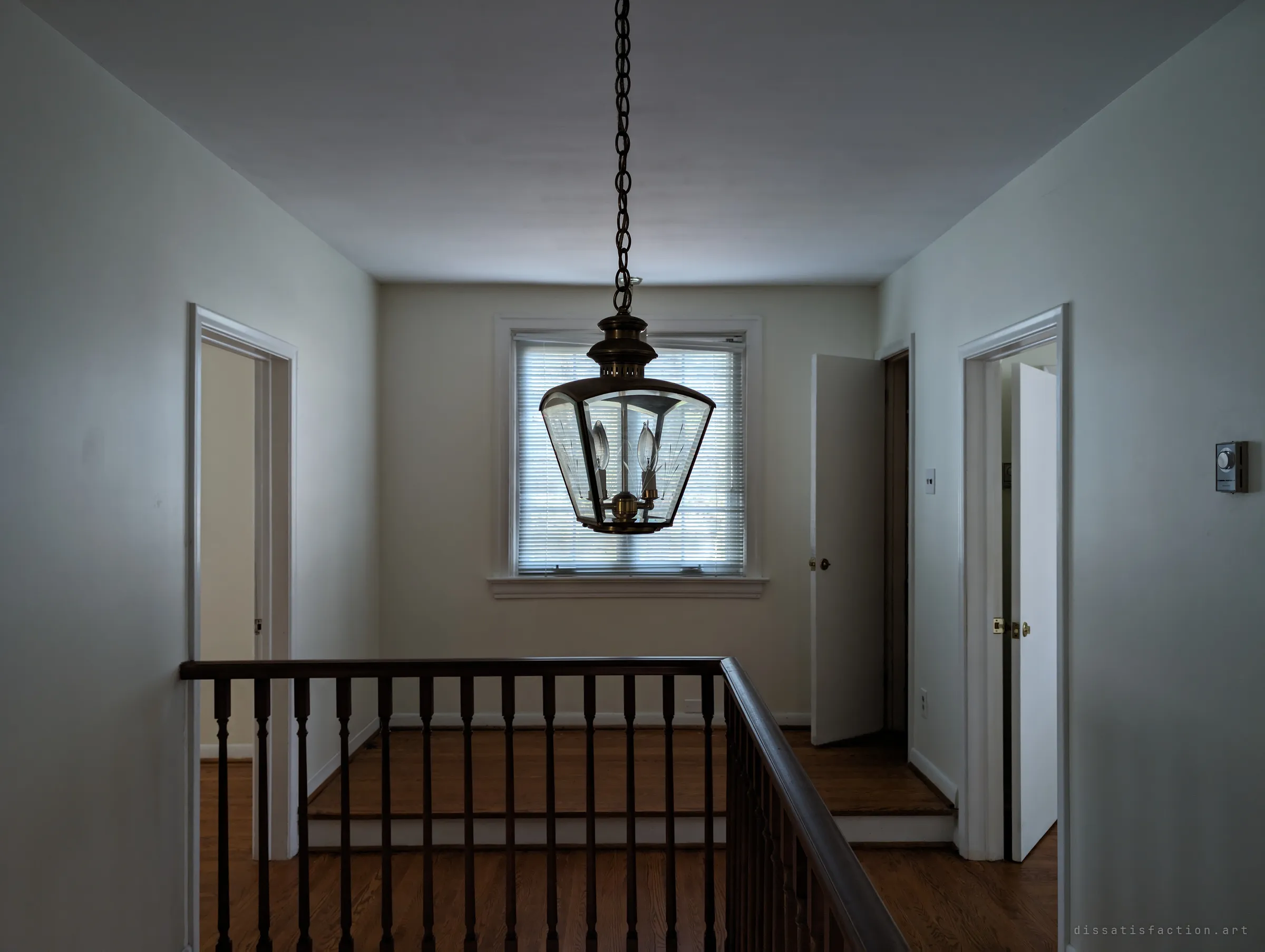 An upstairs landing with a brass-and-glass lantern hanging on a long chain over the stairwell, doors left open to empty rooms. The house looks recently vacated rather than decayed.