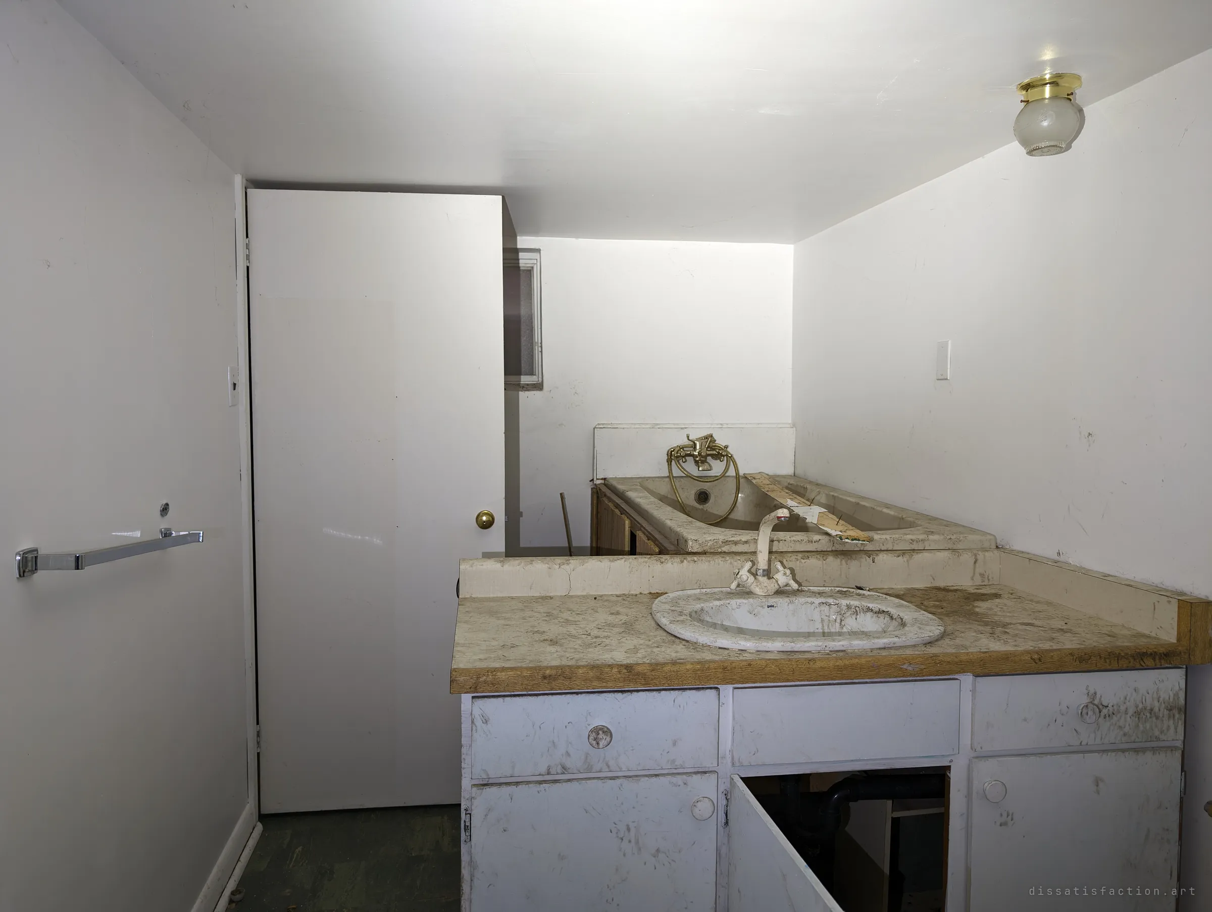 A grimy basement bathroom with a stained vanity sink in front of a bathtub with brass fittings. Dirt and open cabinet doors show years of neglect.